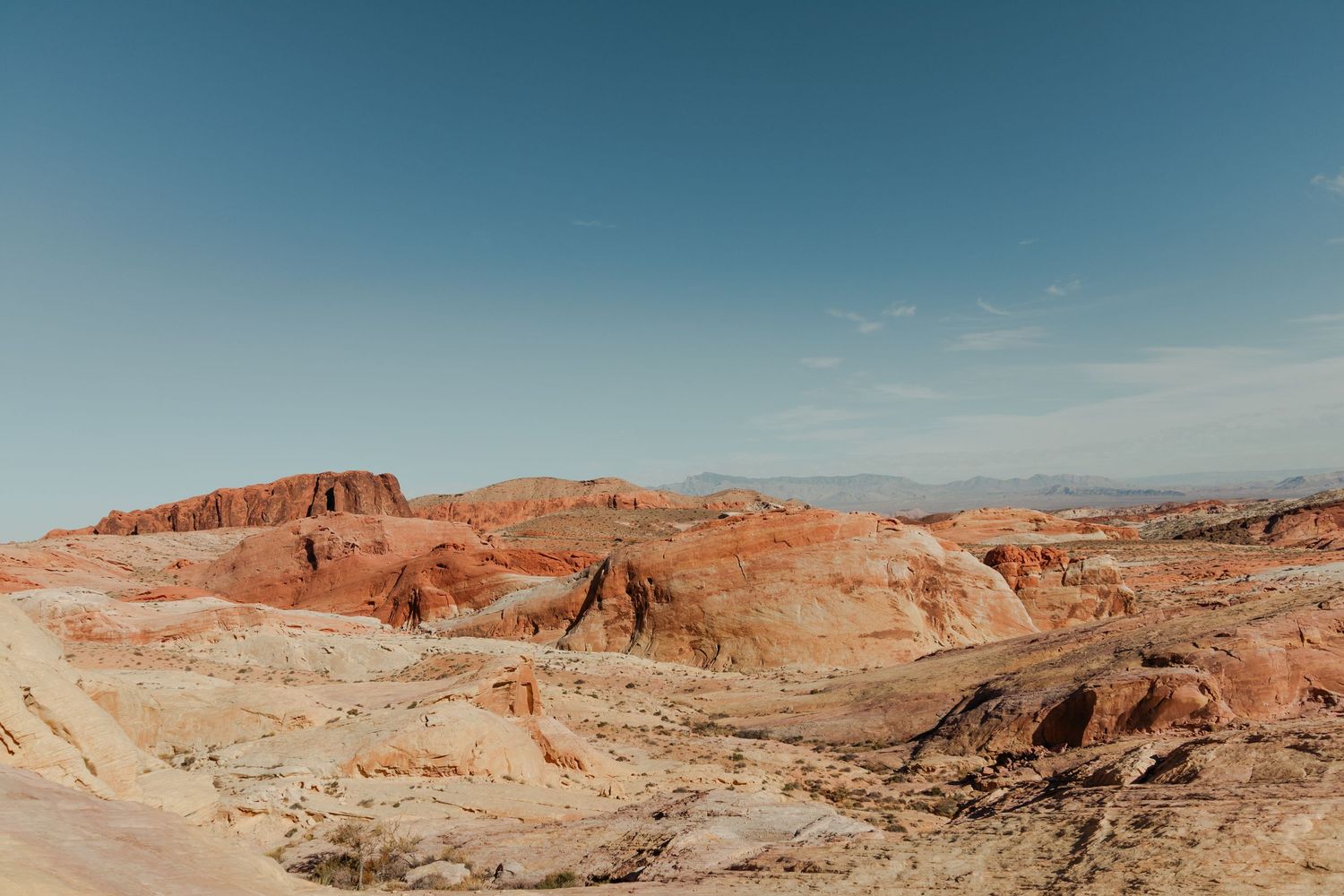 Panoramic view of red rock desert canyon formations under a clear blue sky in an arid southwestern landscape.