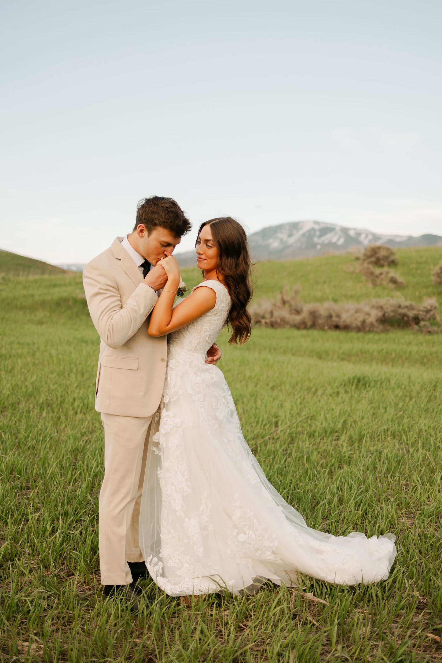 A couple in wedding attire embraces in a scenic mountain meadow.