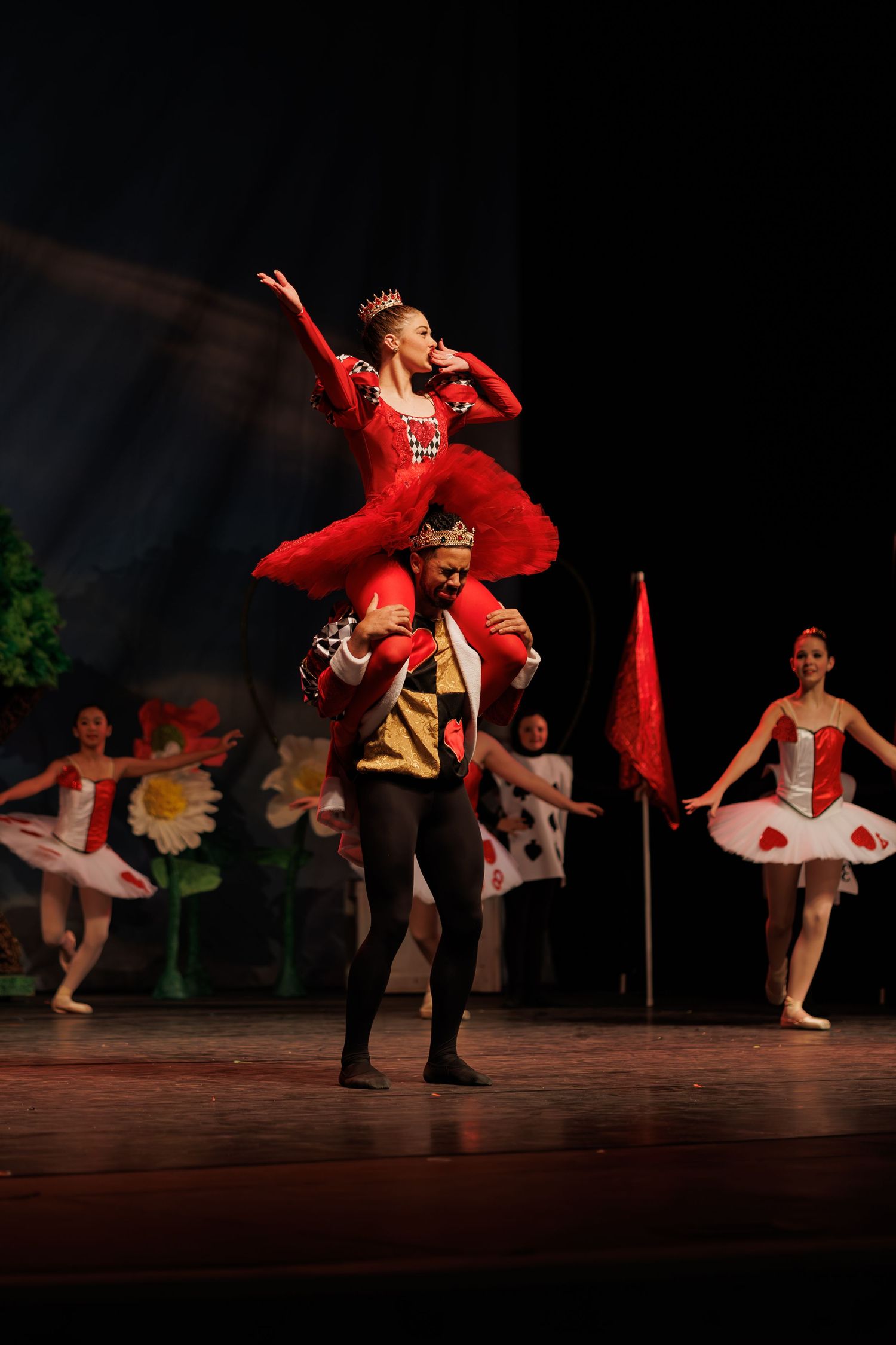 Ballet dancers perform on stage in vibrant red and white costumes during a live theatrical production.