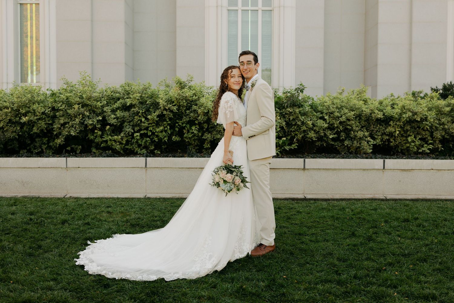 A romantic wedding portrait session on a manicured lawn with white architecture in the background.
