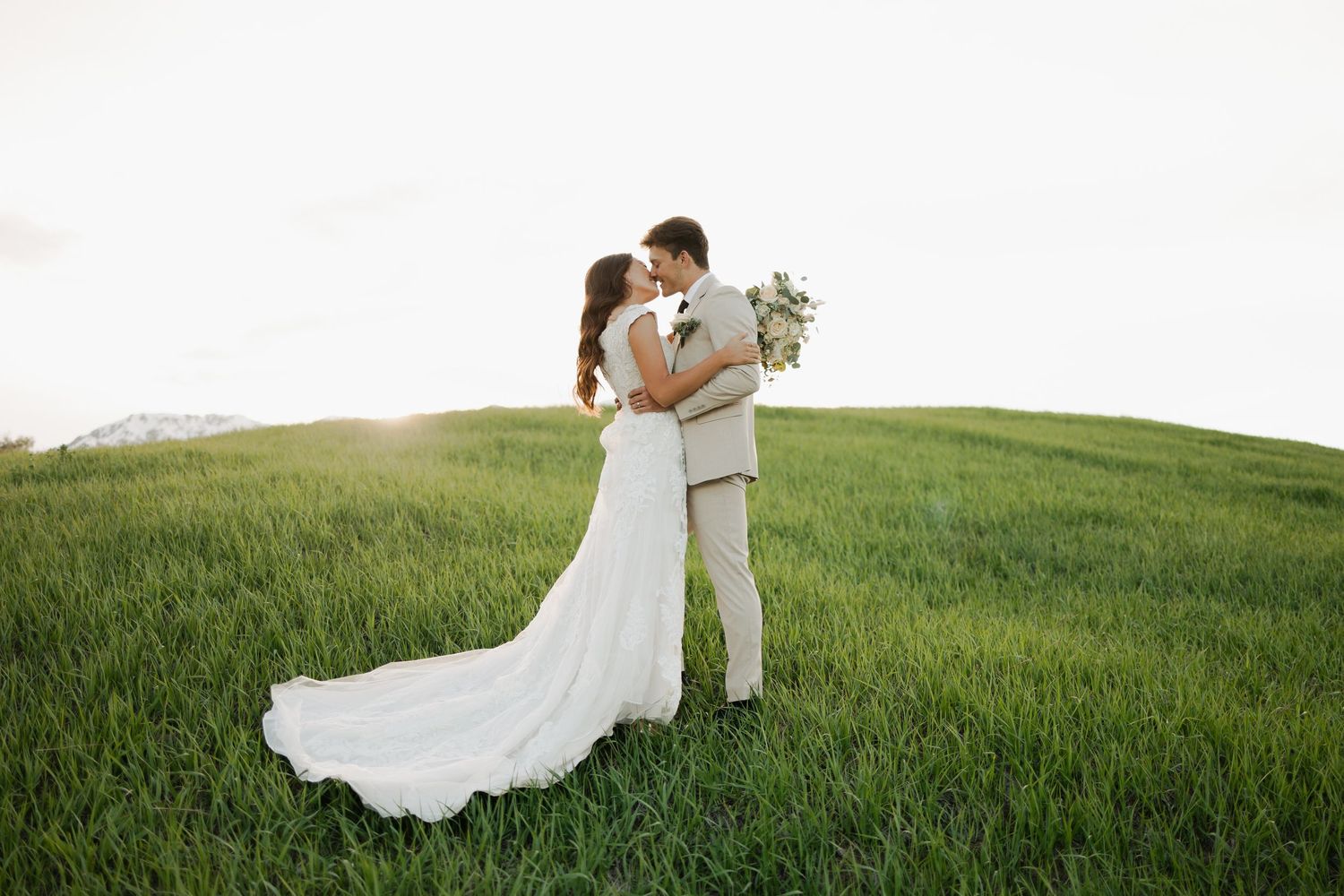A couple poses romantically in a lush green meadow during golden hour.