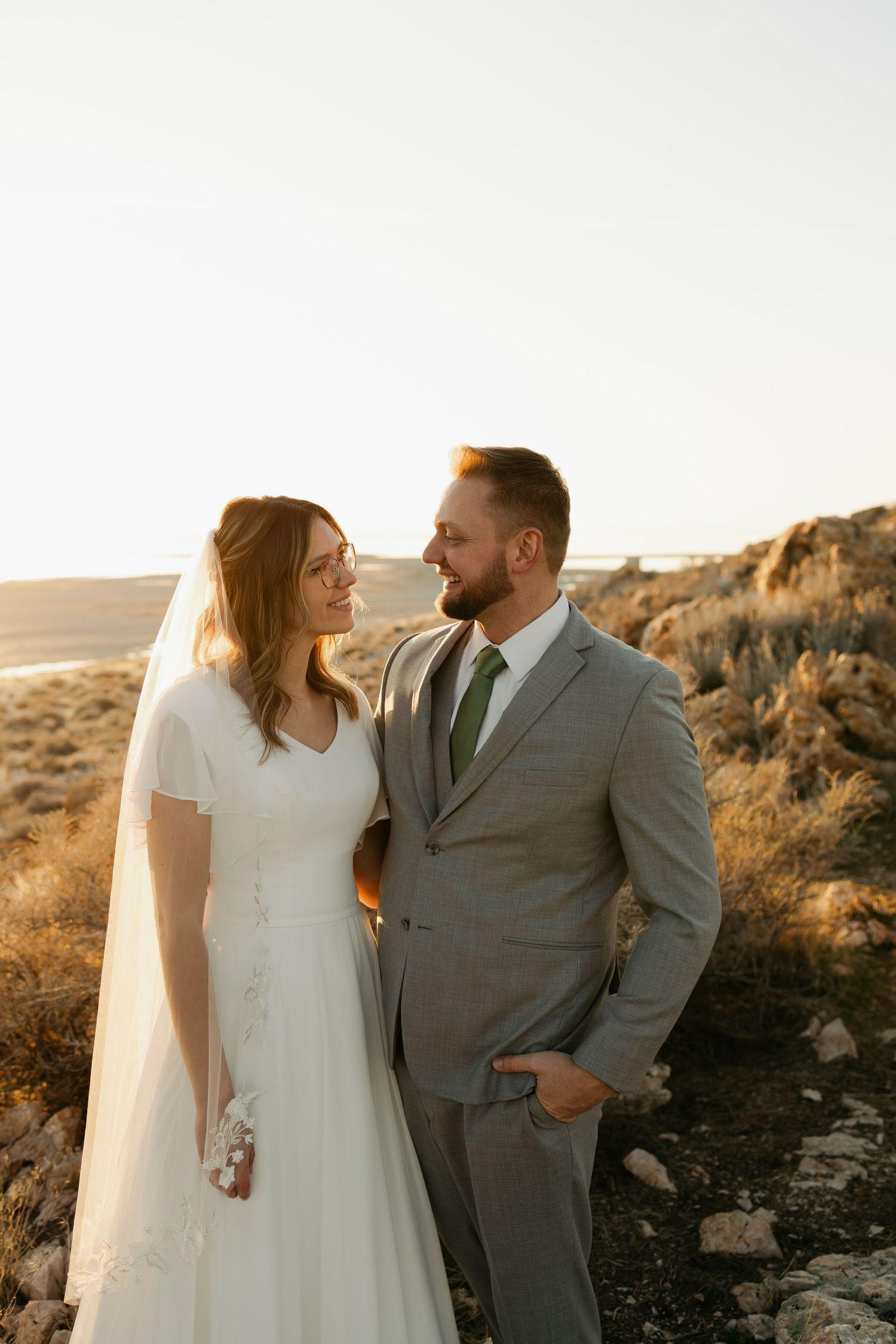 Couple shares tender moments at sunset in a desert setting with mountains in background.