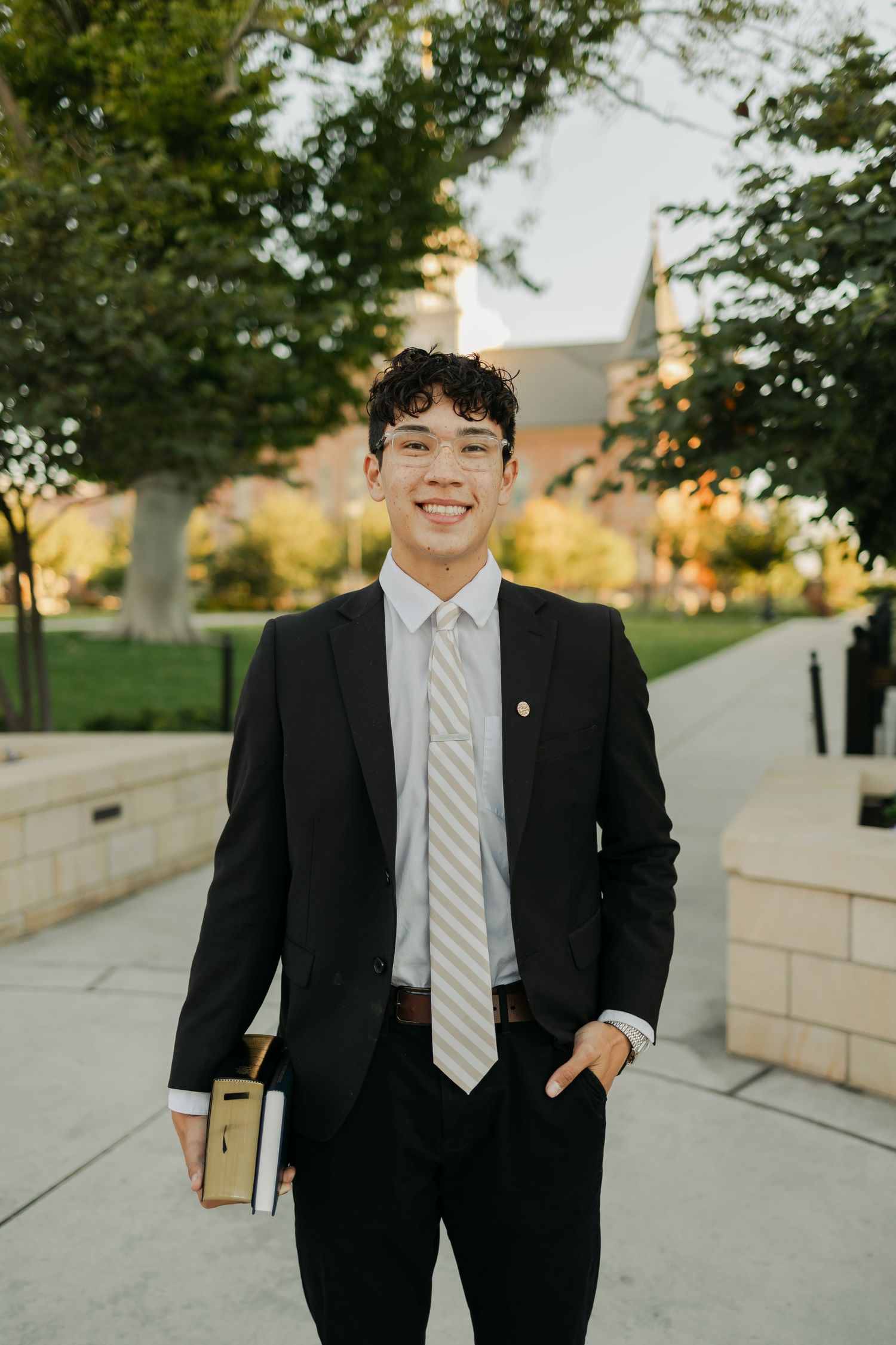 Professional portrait of young graduate in suit and tie standing outdoors at sunset.