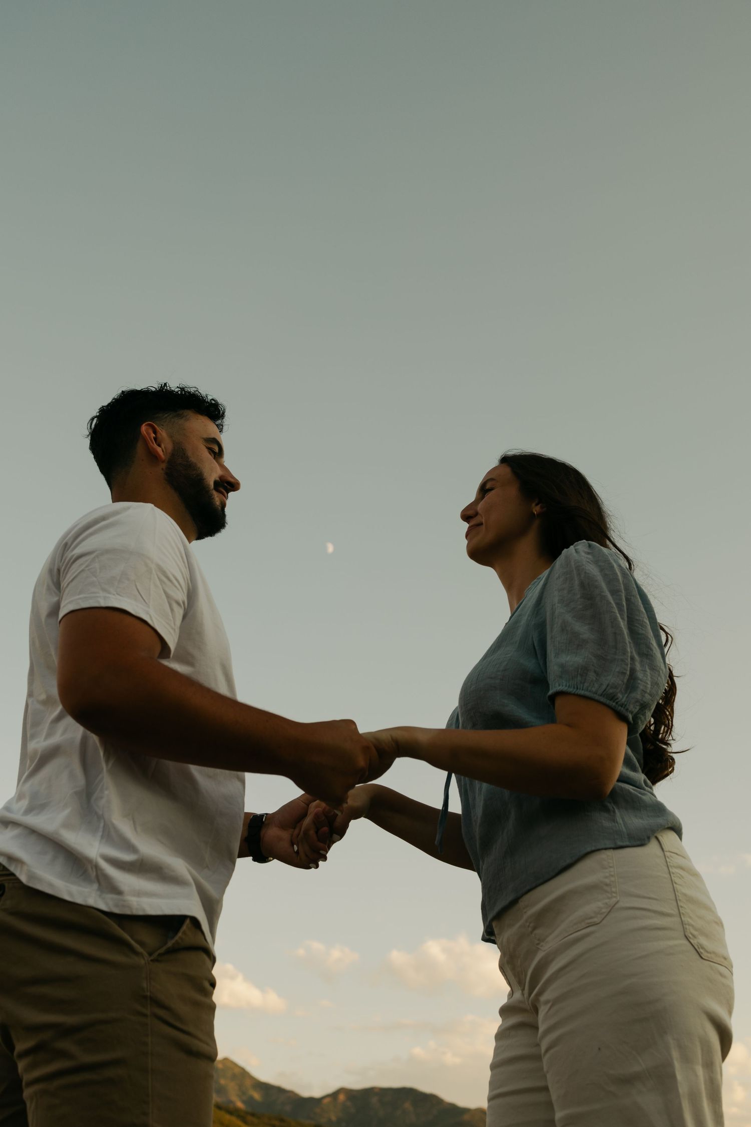 A couple embraces while silhouetted against a sunset sky in a romantic outdoor photo series.