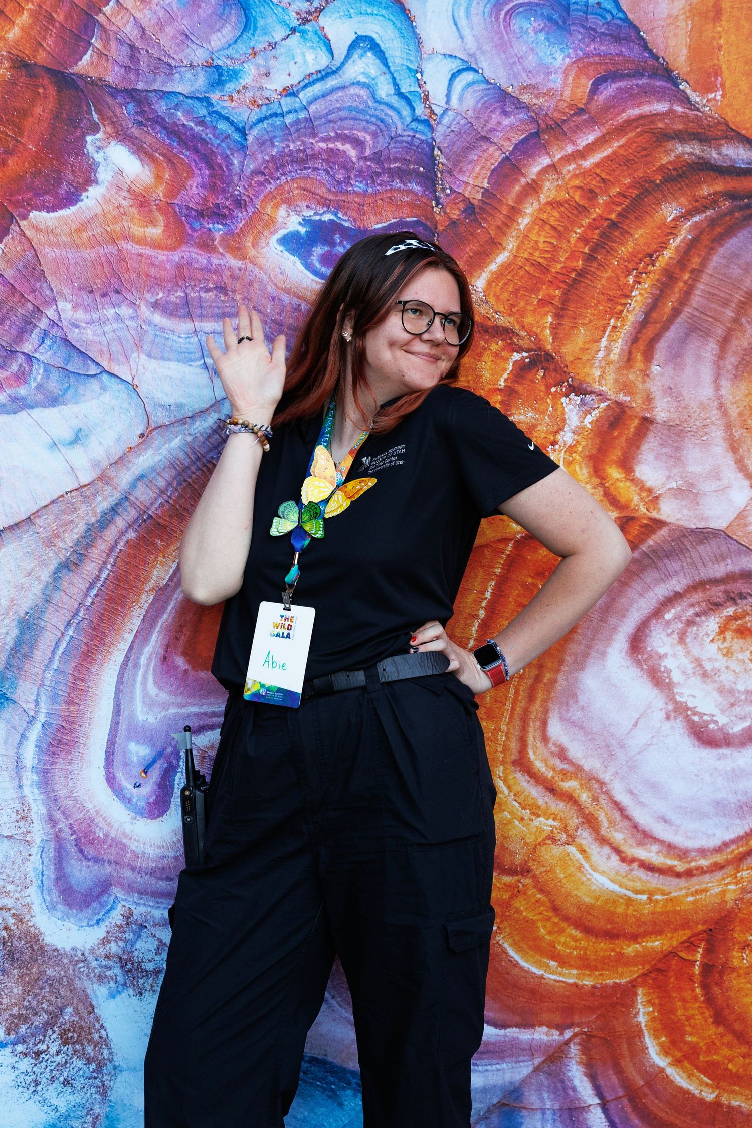 Woman in black uniform with lanyard poses smiling before colorful swirled rock art mural backdrop.