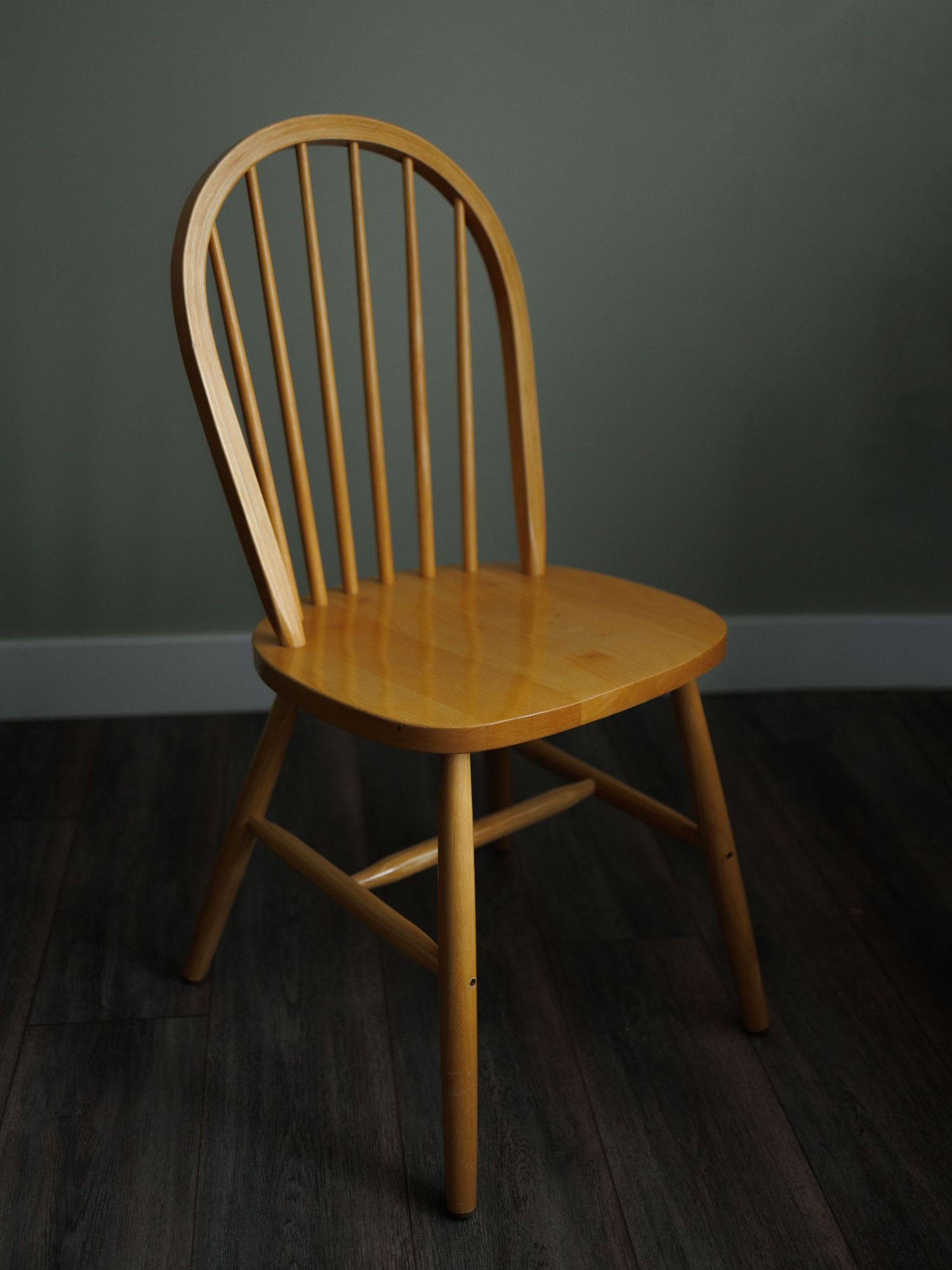 Classic Windsor wooden dining chair with spindle back and natural light oak finish on dark hardwood floor.