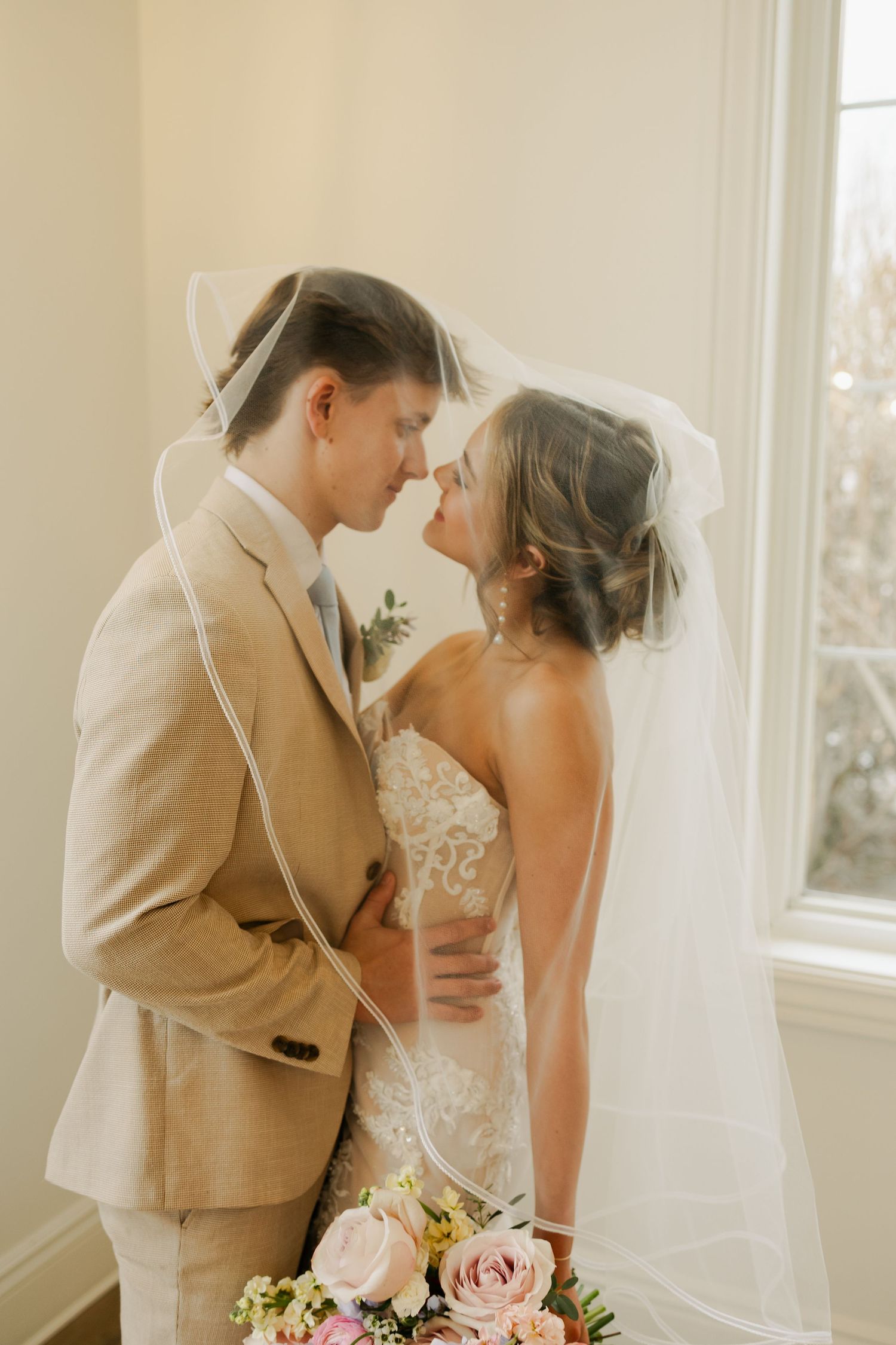 A tender moment between newlyweds by a bright window in an intimate indoor setting.