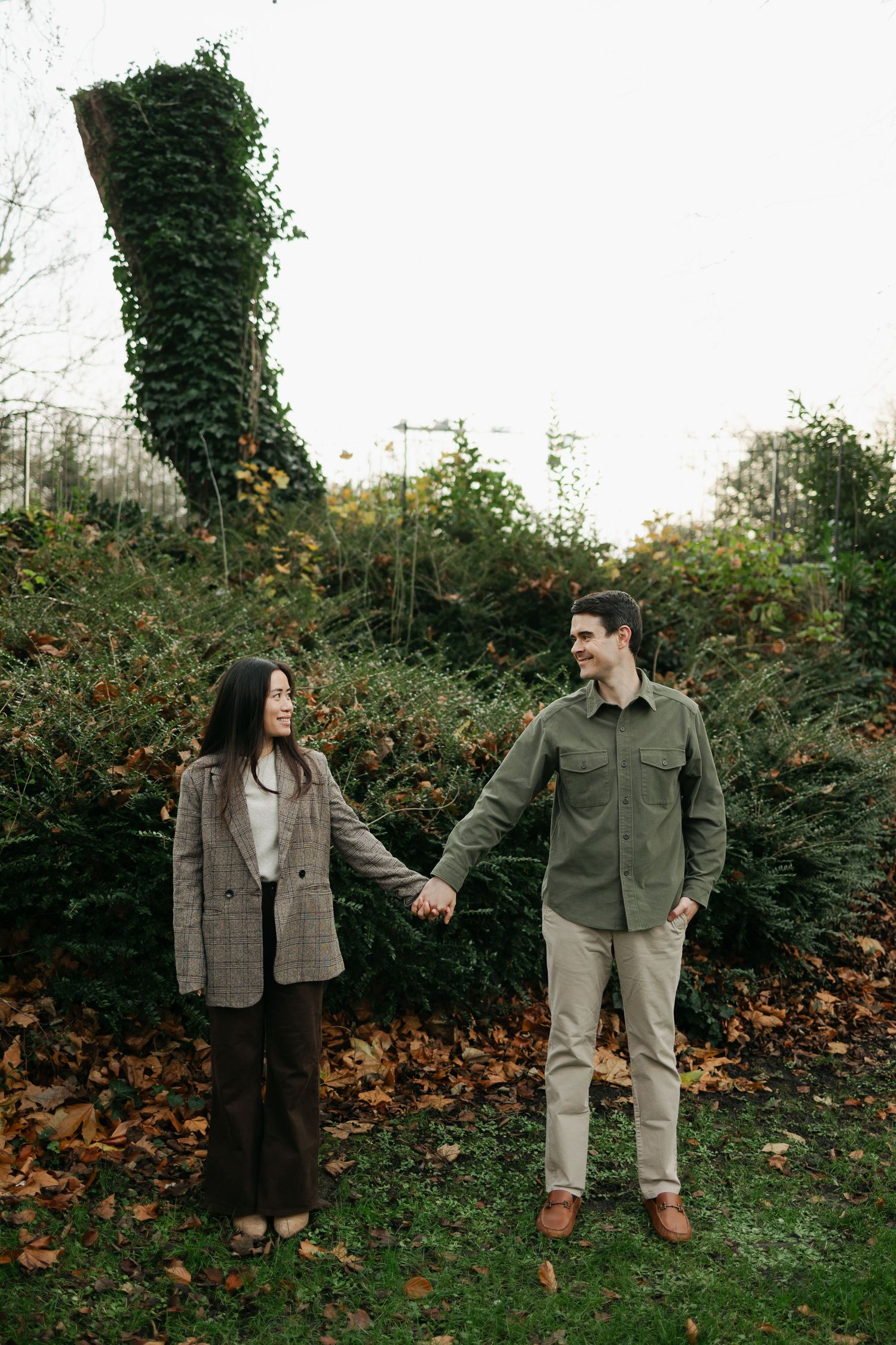 Couple holding hands in an autumn garden with ivy-covered trees and fallen leaves.