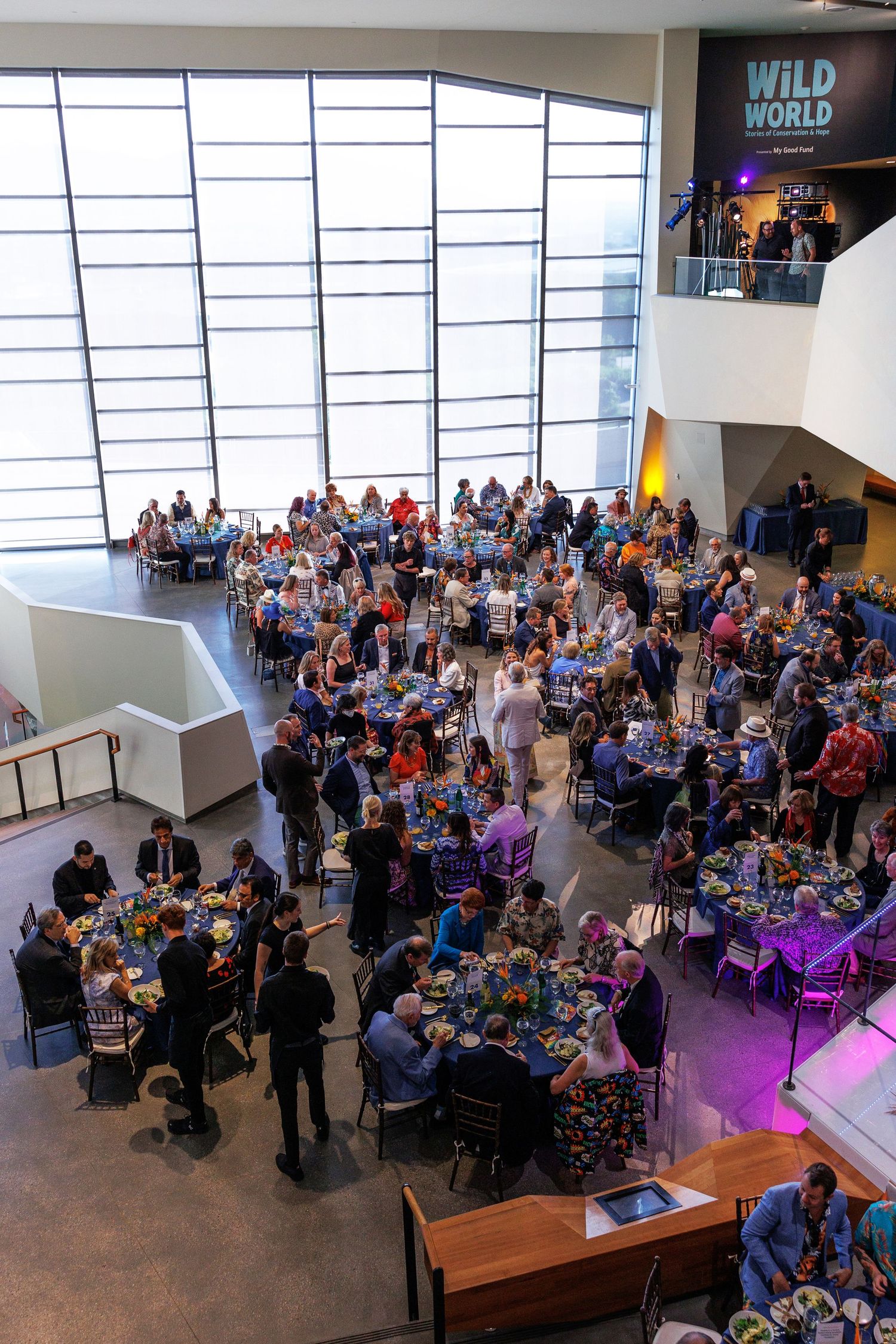 Aerial view of a large gala event with guests seated at round tables in a modern museum atrium.