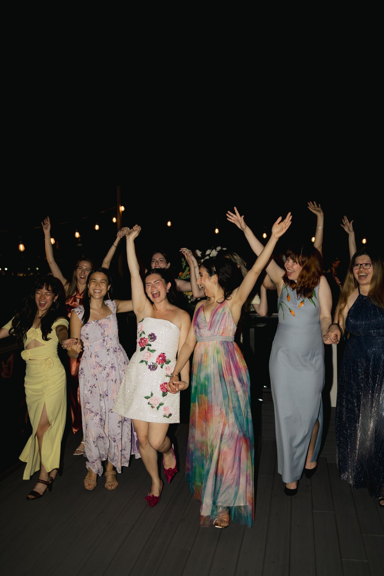 A group of party guests dancing and raising their arms joyfully at a nighttime outdoor celebration.