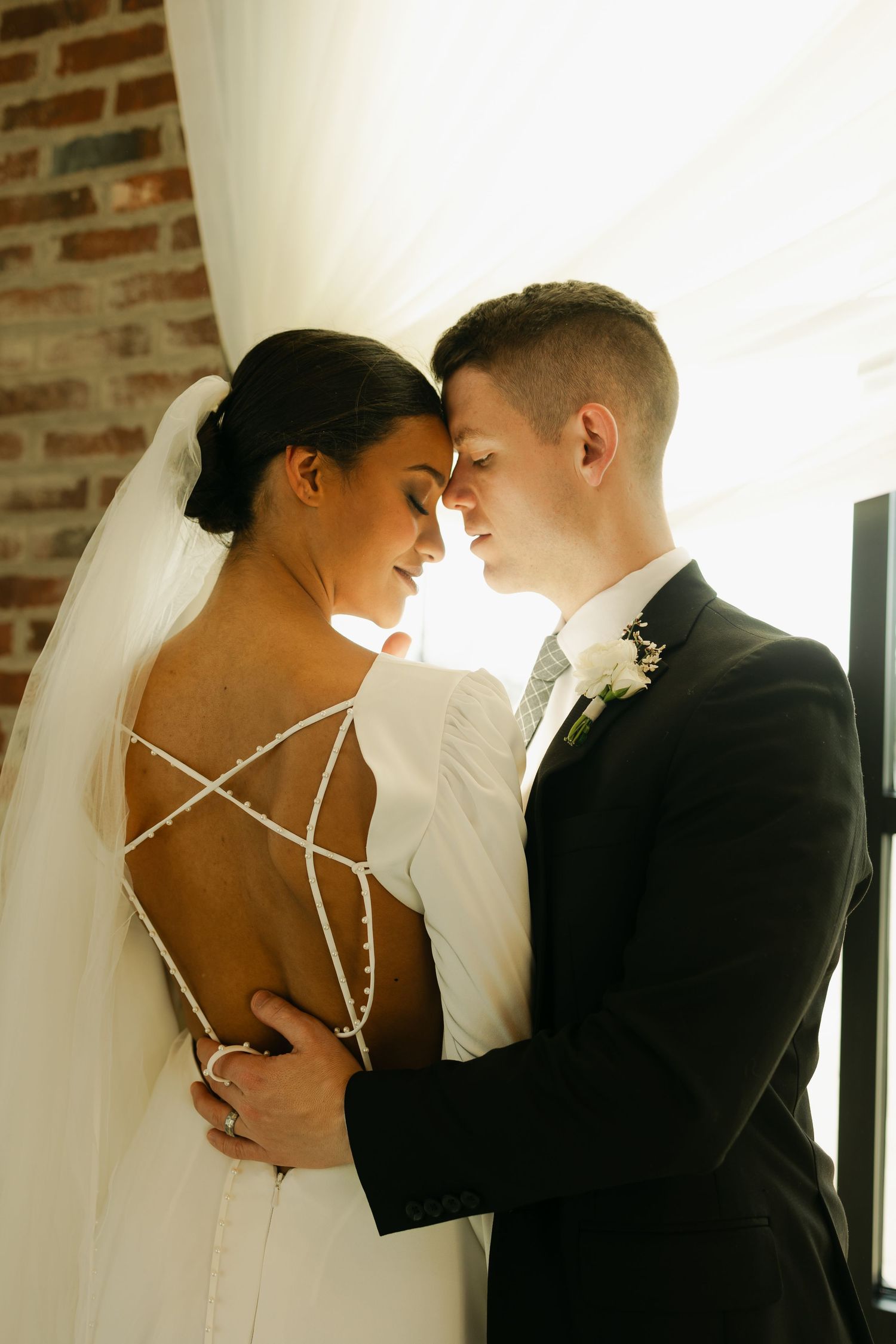An intimate wedding portrait capturing a tender moment in front of a brick wall.