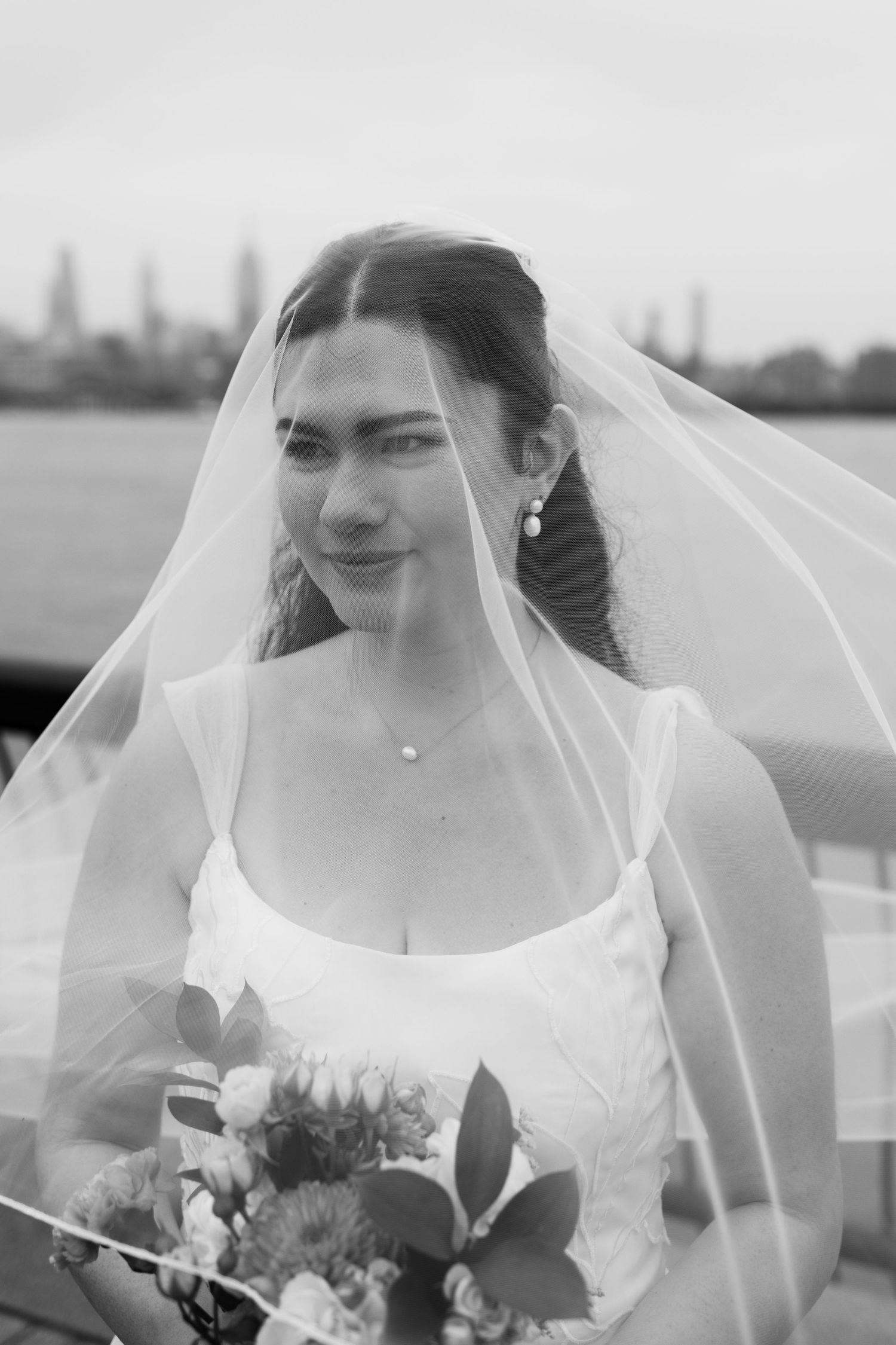 Black and white portrait of bride wearing veil with city skyline in background.