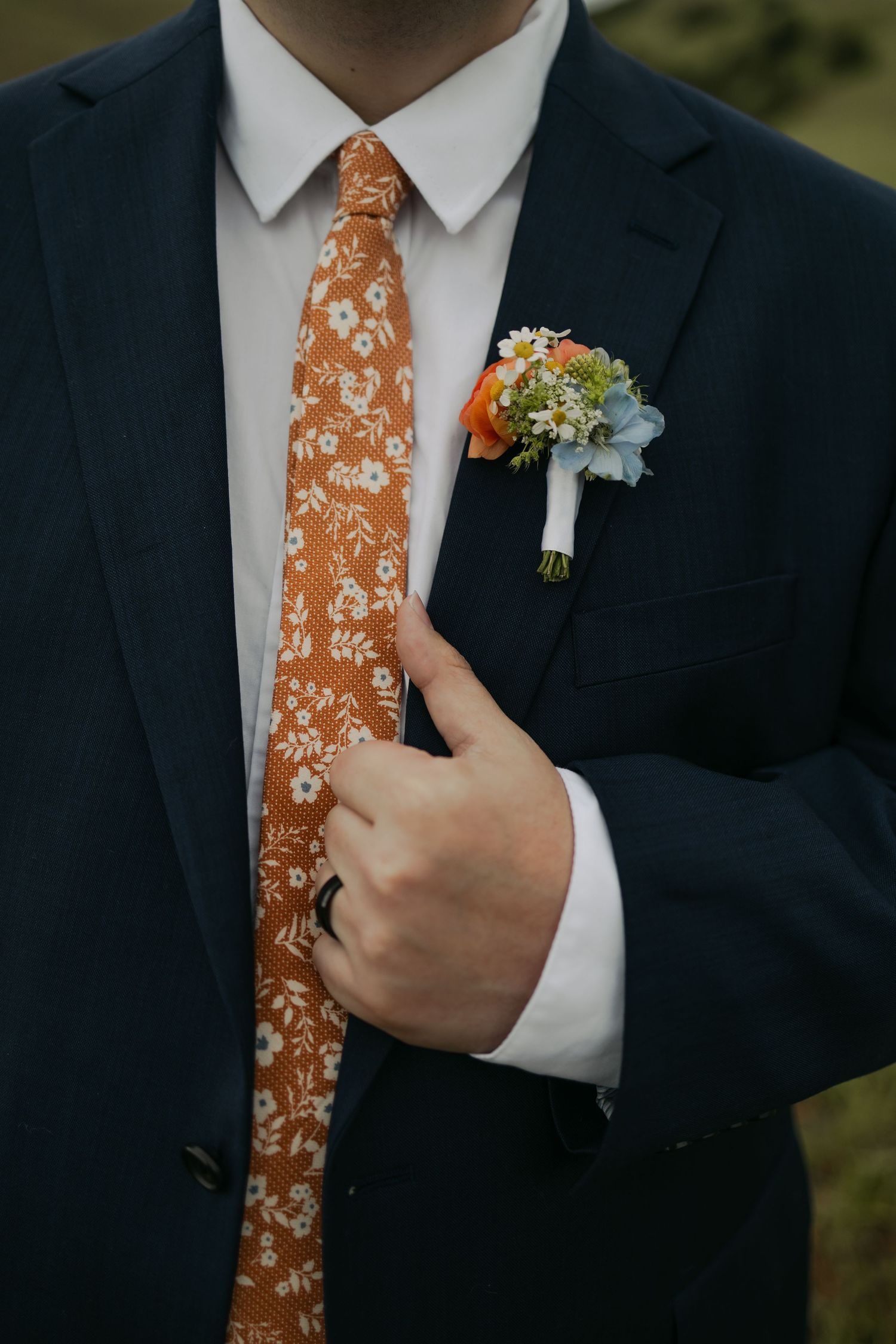 Groom in navy suit with orange floral tie and boutonniere of blue and orange flowers at wedding.
