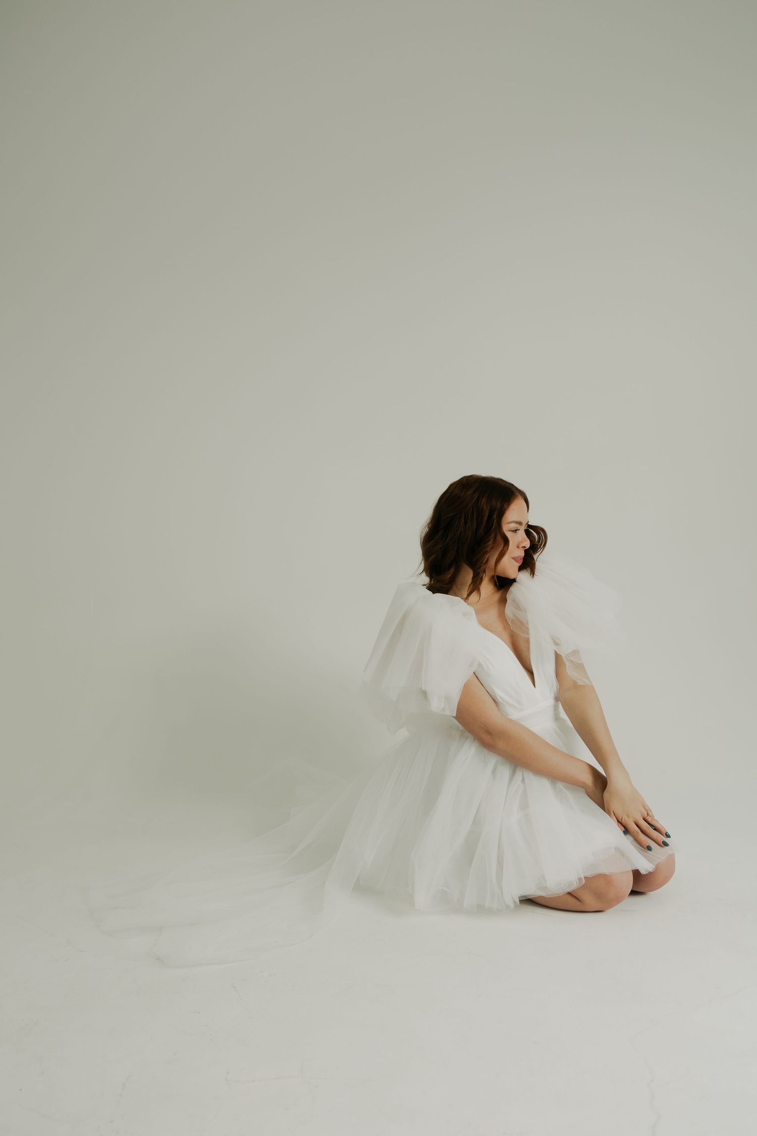 Artistic minimalist portrait of figure in white dress against light grey backdrop.