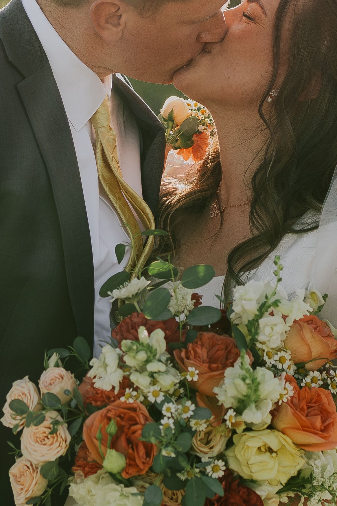 A romantic wedding photo showing a couple kissing behind a stunning bouquet of peach and cream roses.