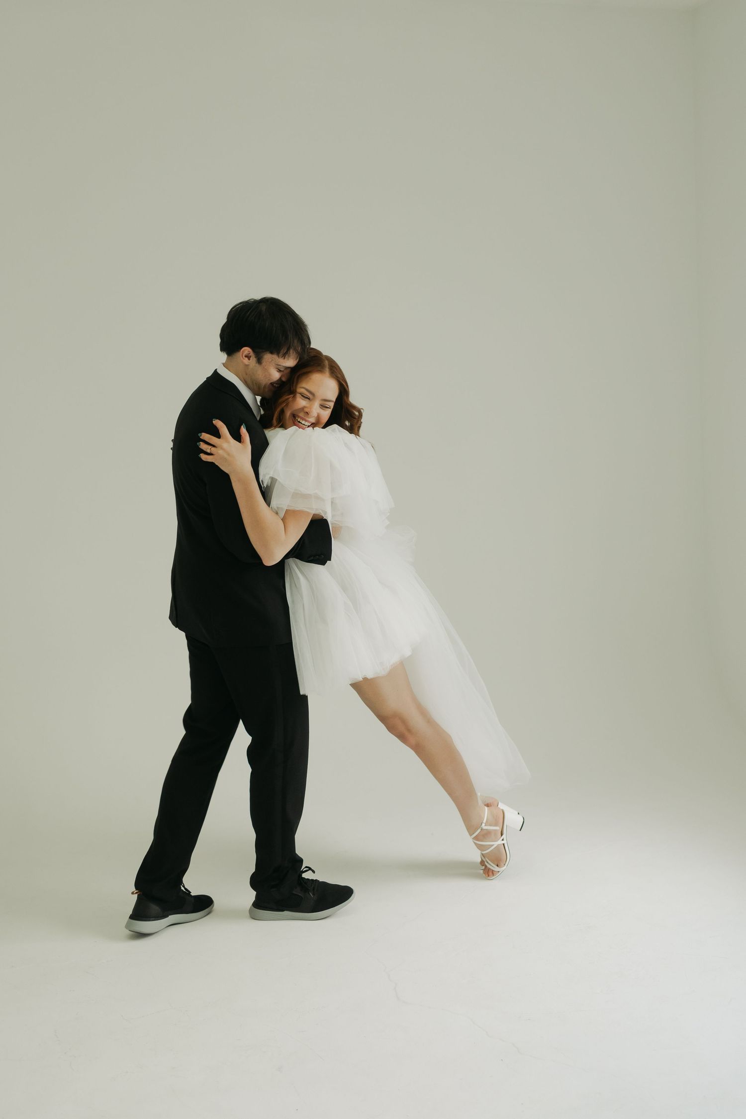 Two people in formal attire share intimate dance poses in black and white studio setting.