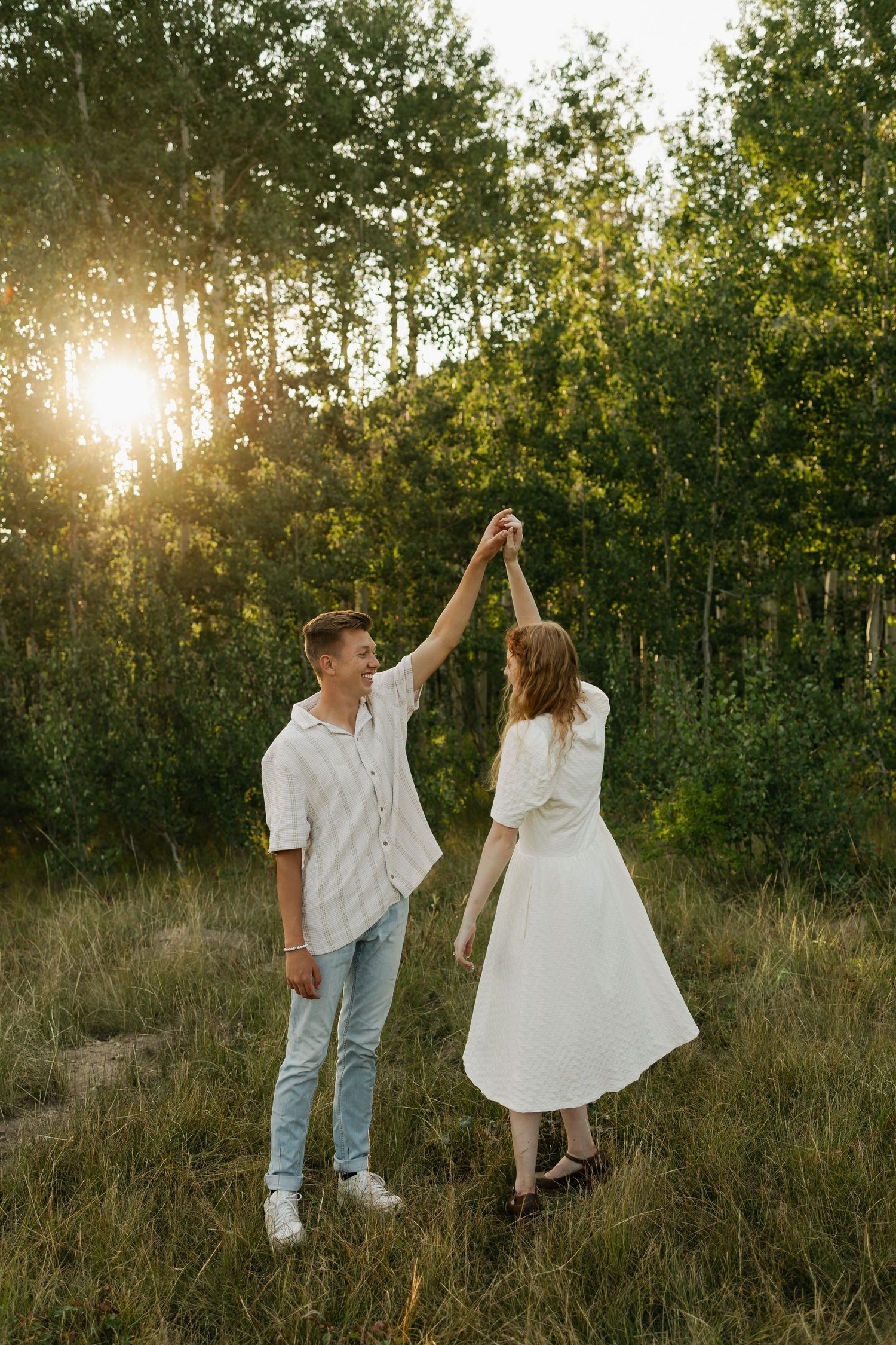 A couple dances and twirls in a sun-drenched field during golden hour.