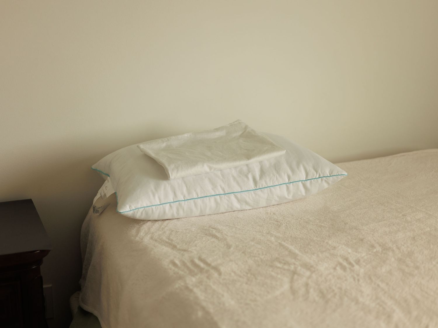 Single bed with white bedding and two pillows, neatly made in a minimalist bedroom setting.