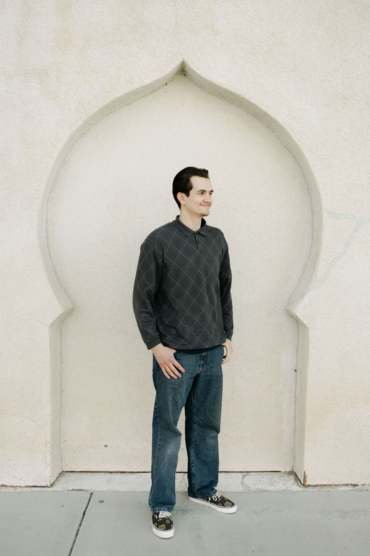 A person poses dynamically against white architectural arches in casual attire.