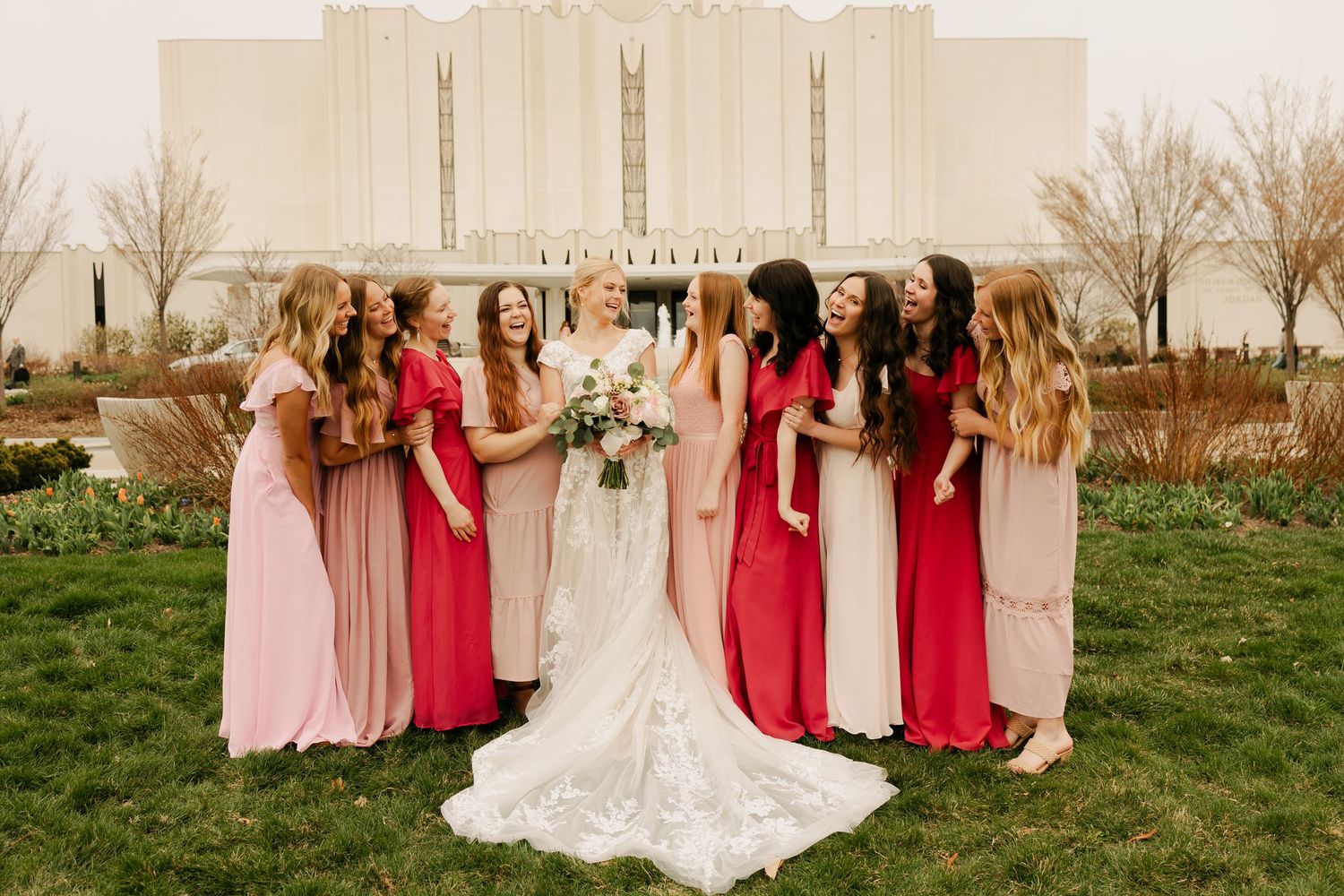 Wedding party with bridesmaids in pink and red dresses posing in front of a modern building.