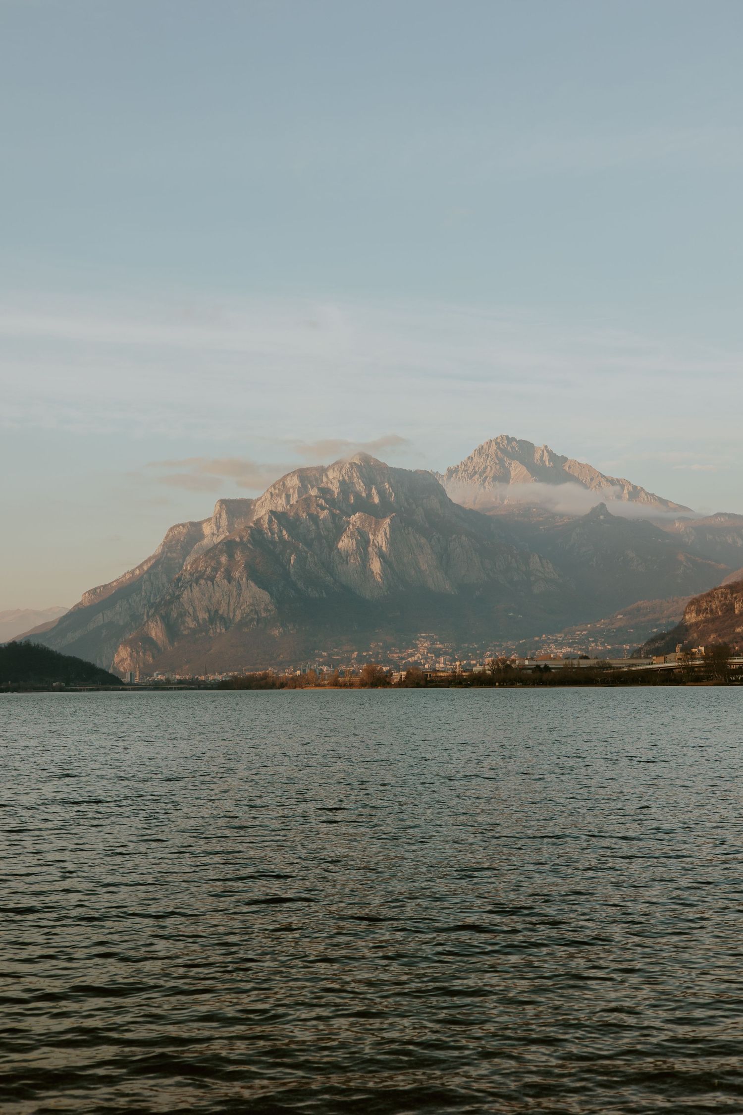 Serene alpine lake with dramatic mountain peaks reflected in calm waters under a soft pastel sky at golden hour.