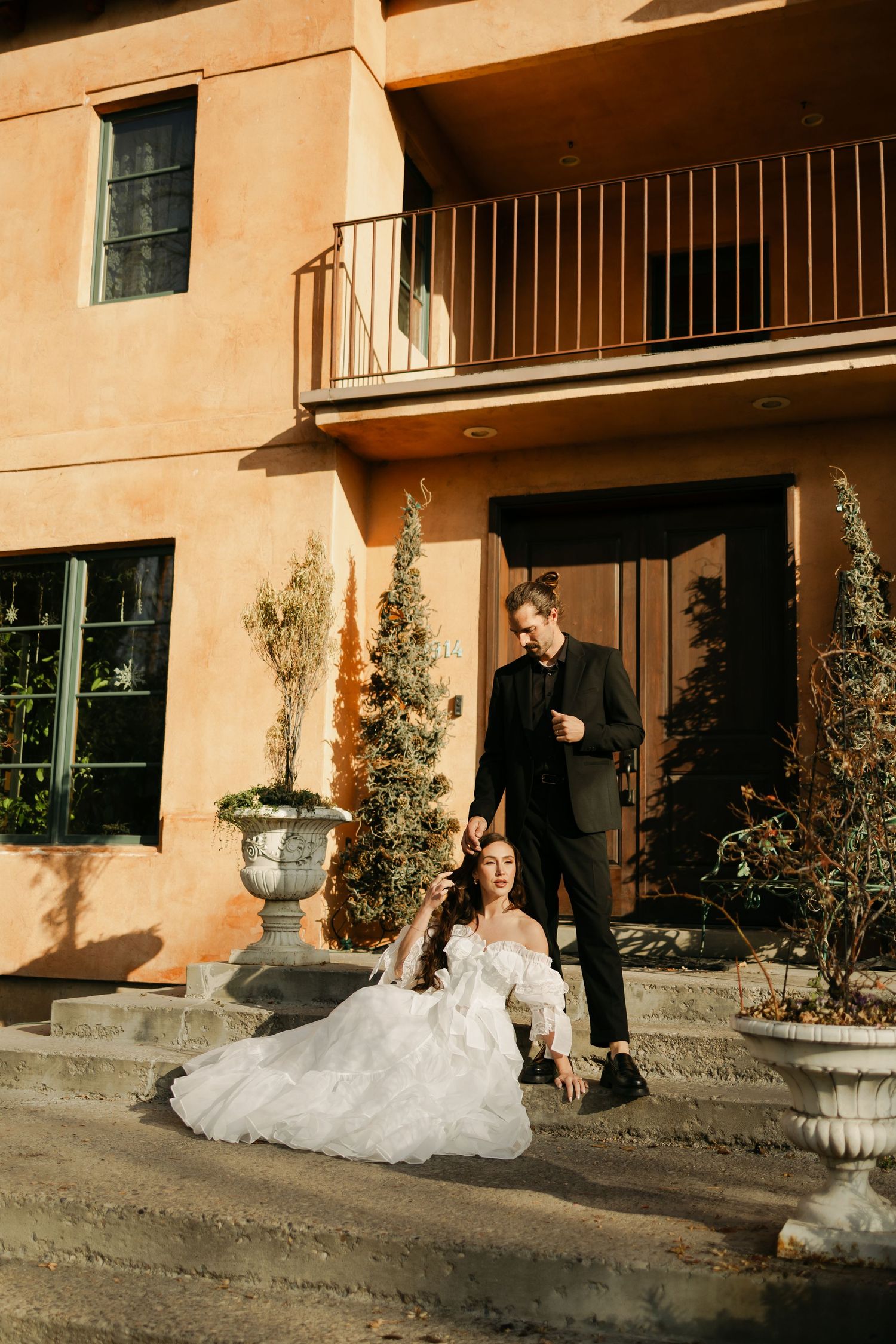Wedding couple poses dramatically outside a Mediterranean-style building with ornate details.