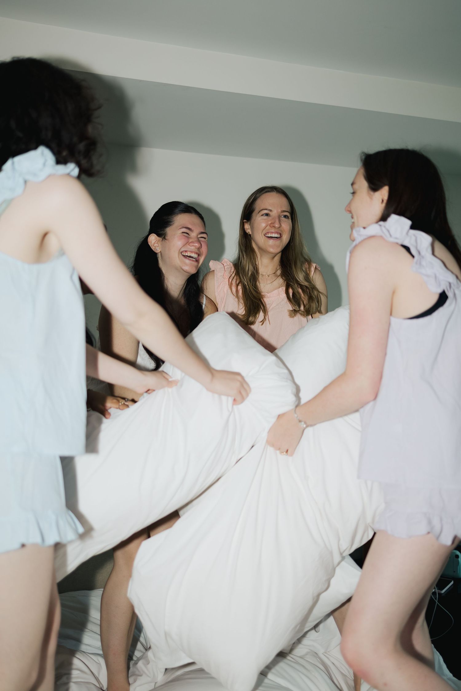 A group of friends in white clothing having fun and laughing while having a pillow fight in a bedroom.