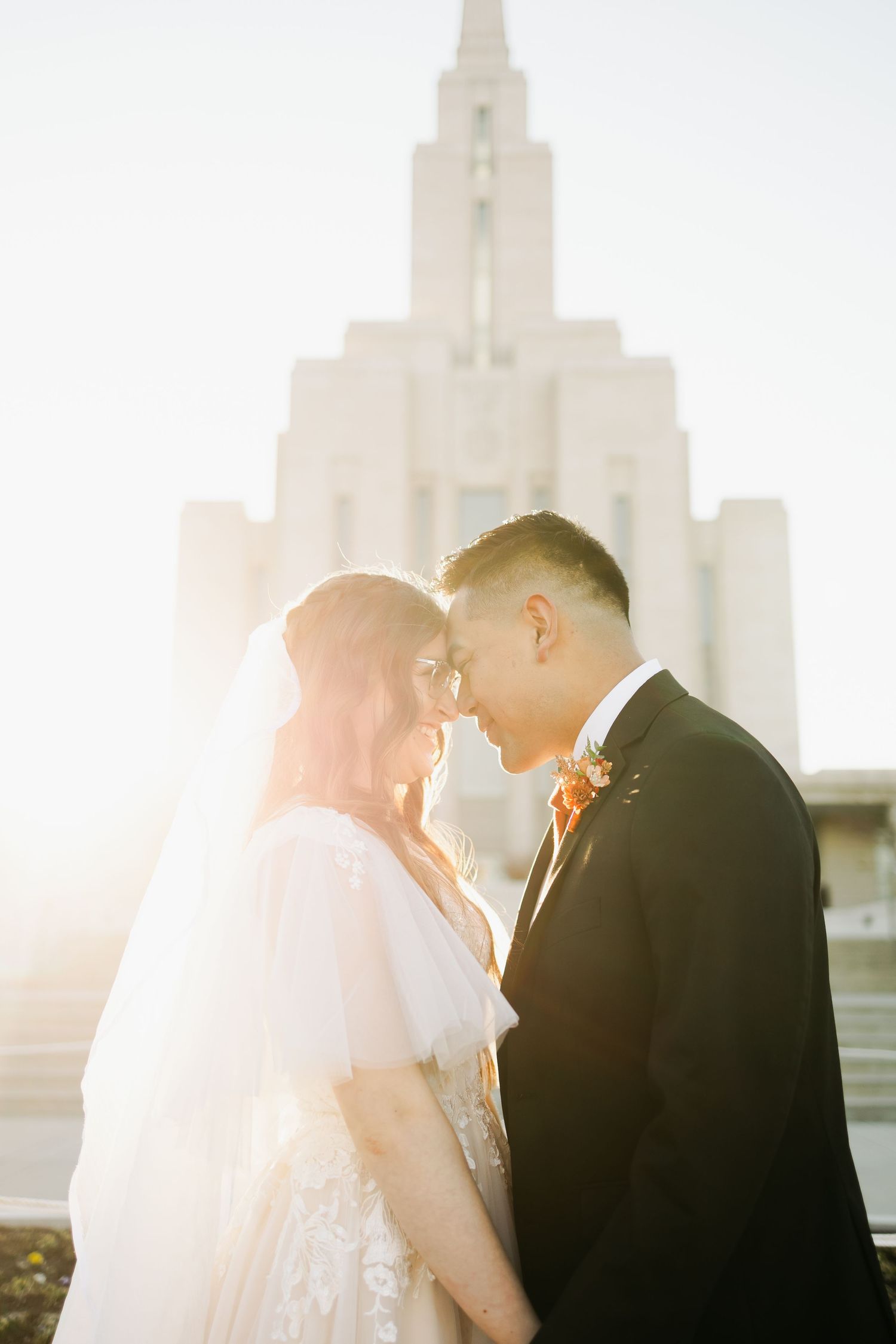 Romantic wedding couple embraces in silhouette against glowing sunset with church steeples in background.