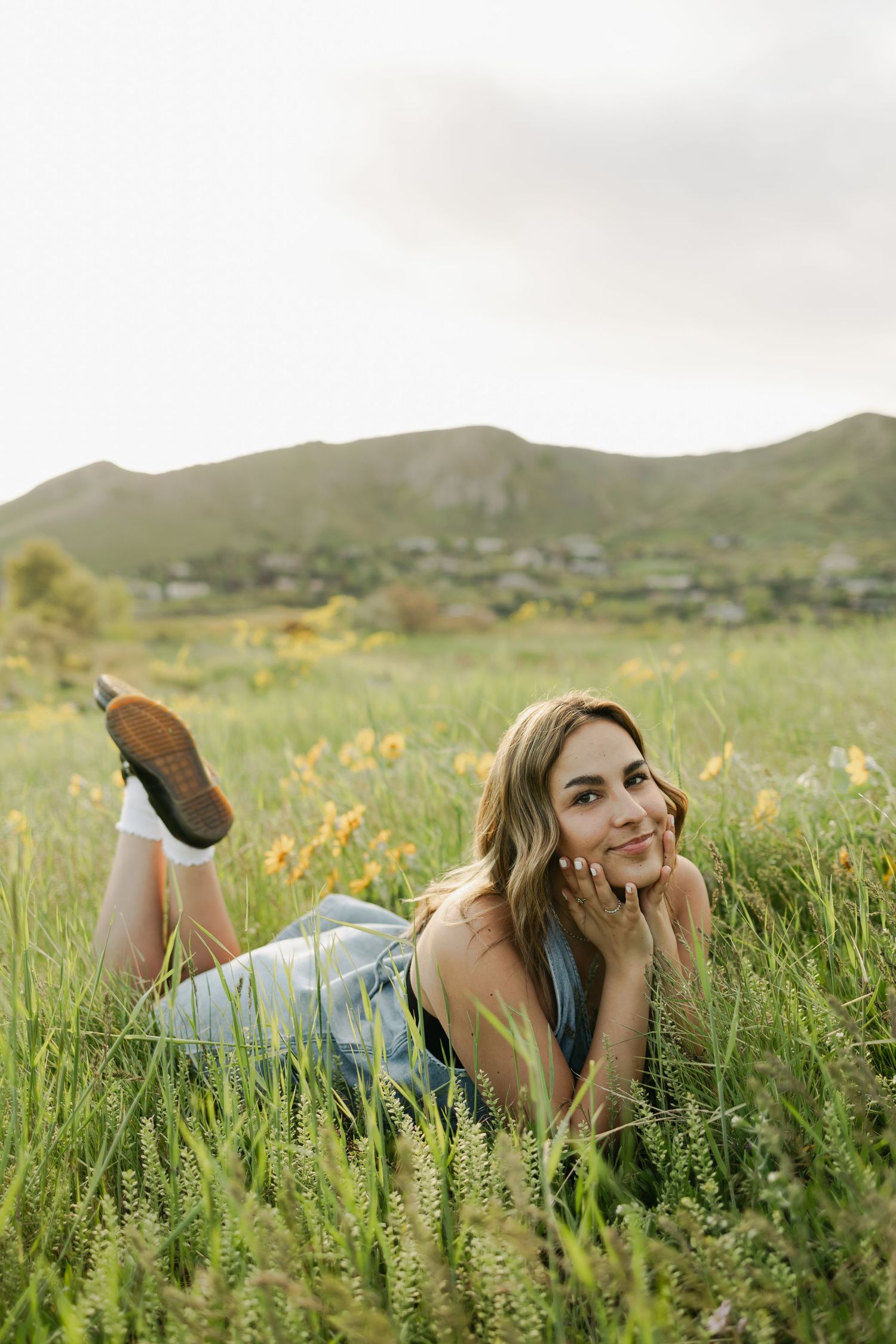 Person lying in wildflower meadow with mountains in background during golden hour.