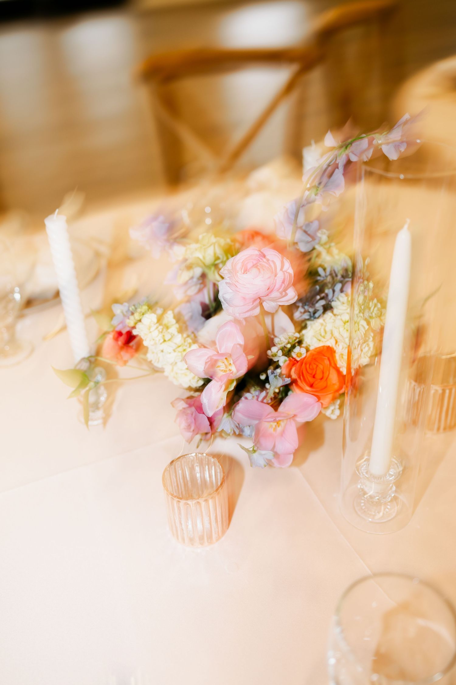 Soft focus table setting with pink and coral floral centerpiece and crystal glassware.
