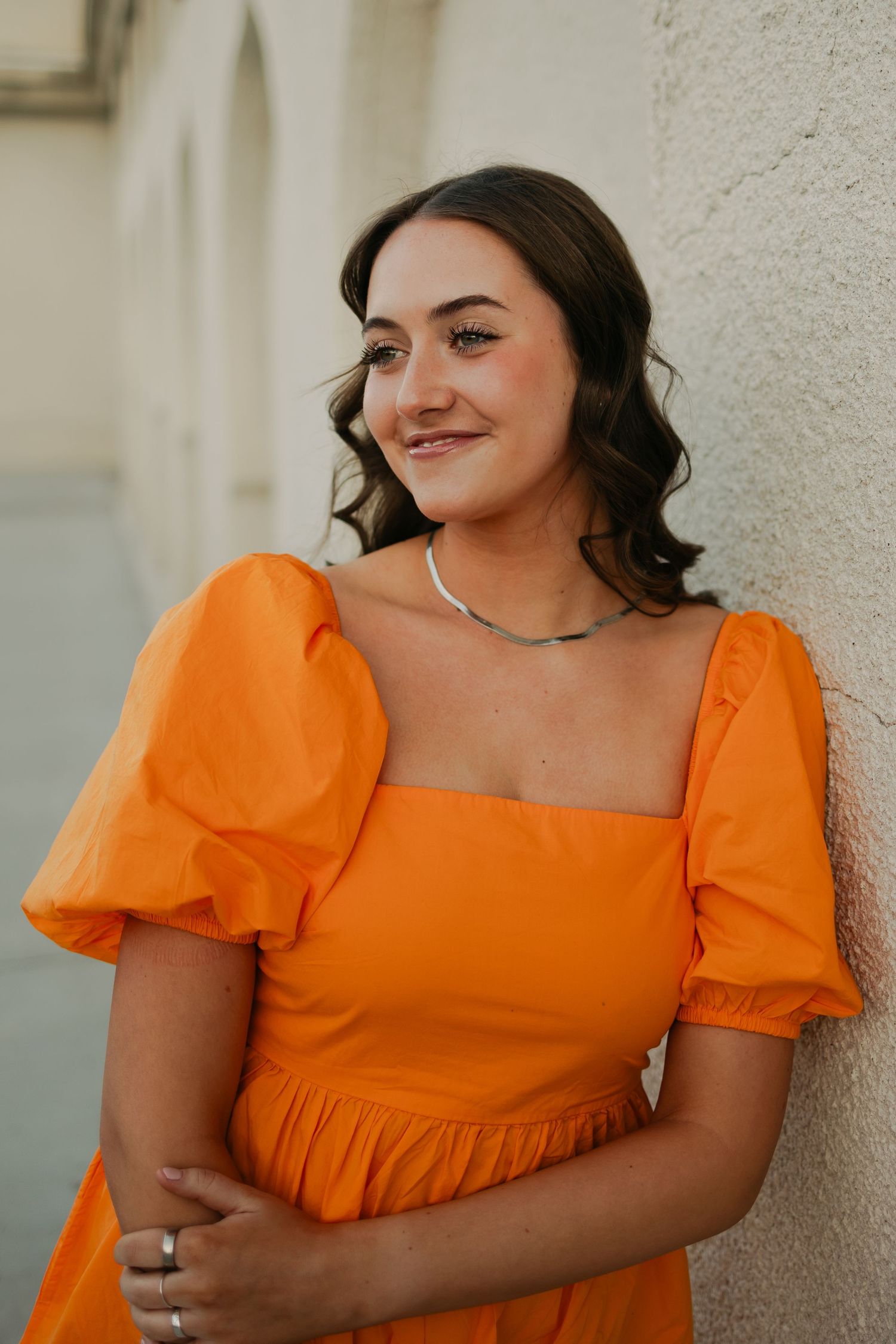 Portrait against white wall wearing bright orange dress with puff sleeves.