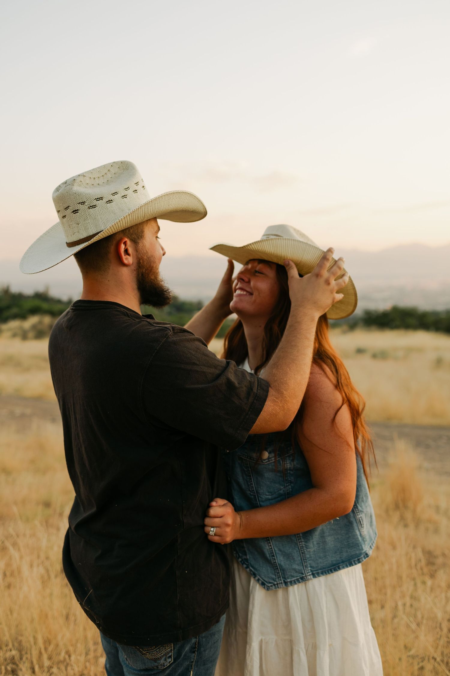 Couple in western attire sharing romantic moment in golden field at sunset.