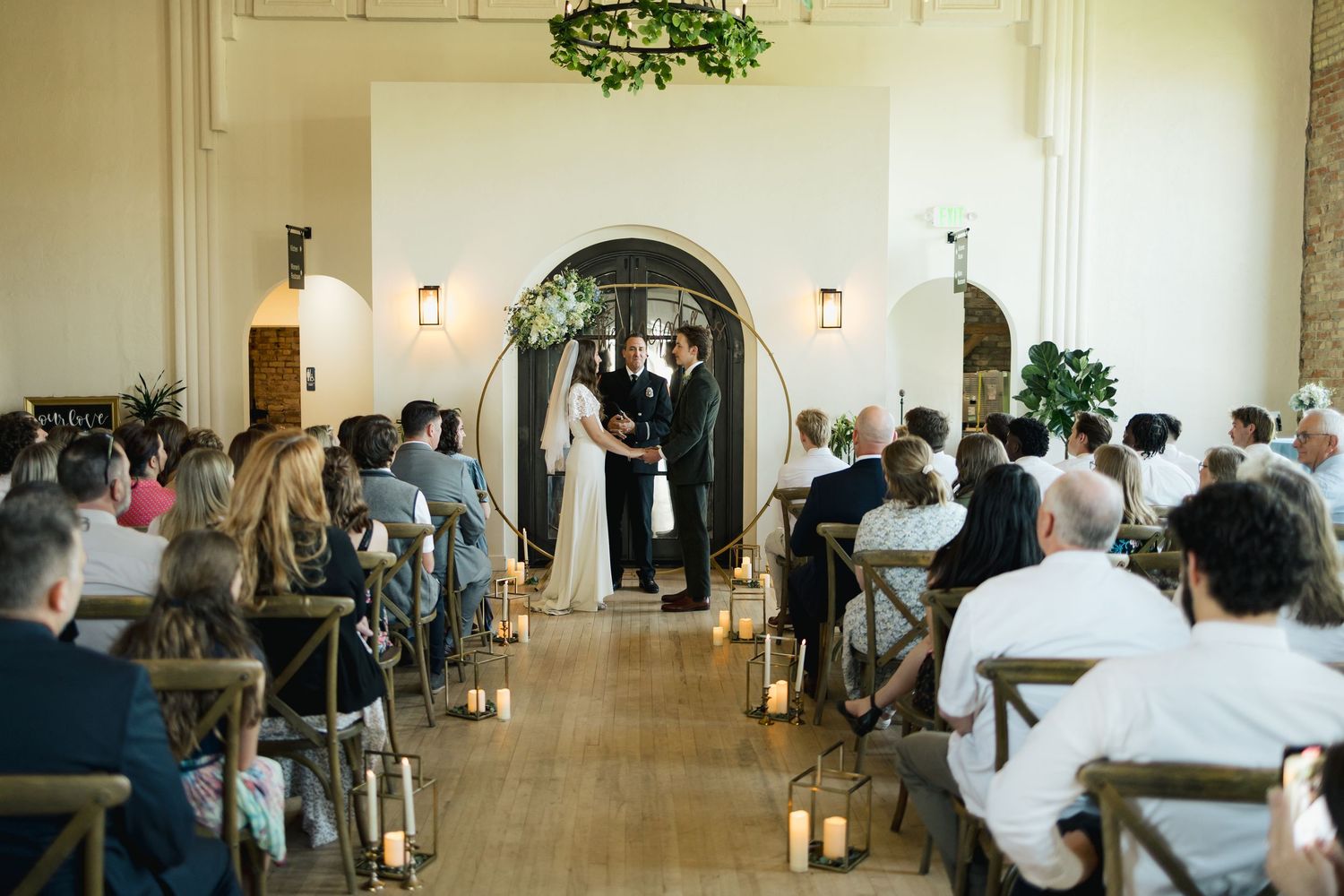 Church wedding ceremony in a bright white interior with guests seated in rows.