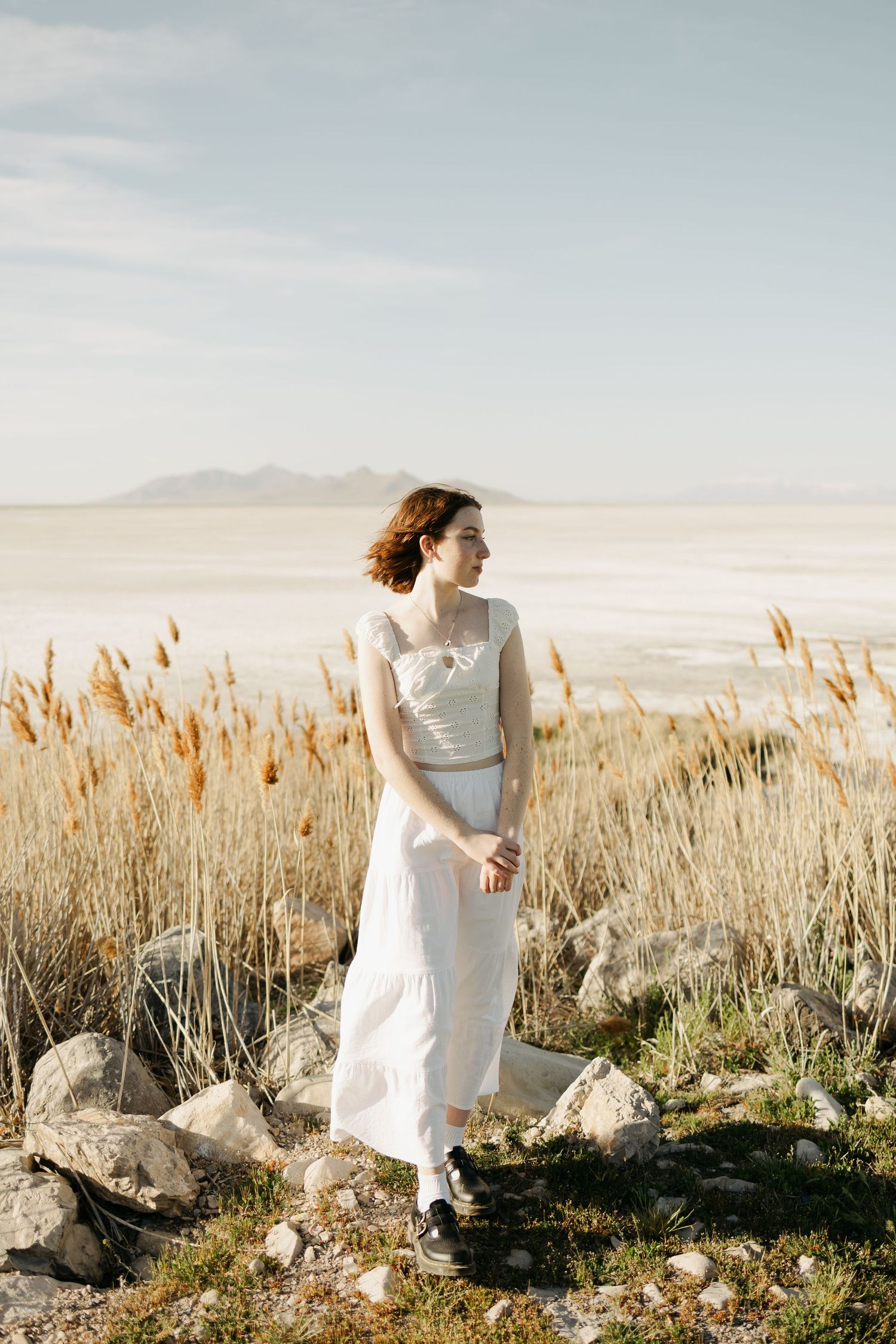 Figure in flowing white dress dancing through a field of tall grass at sunset.