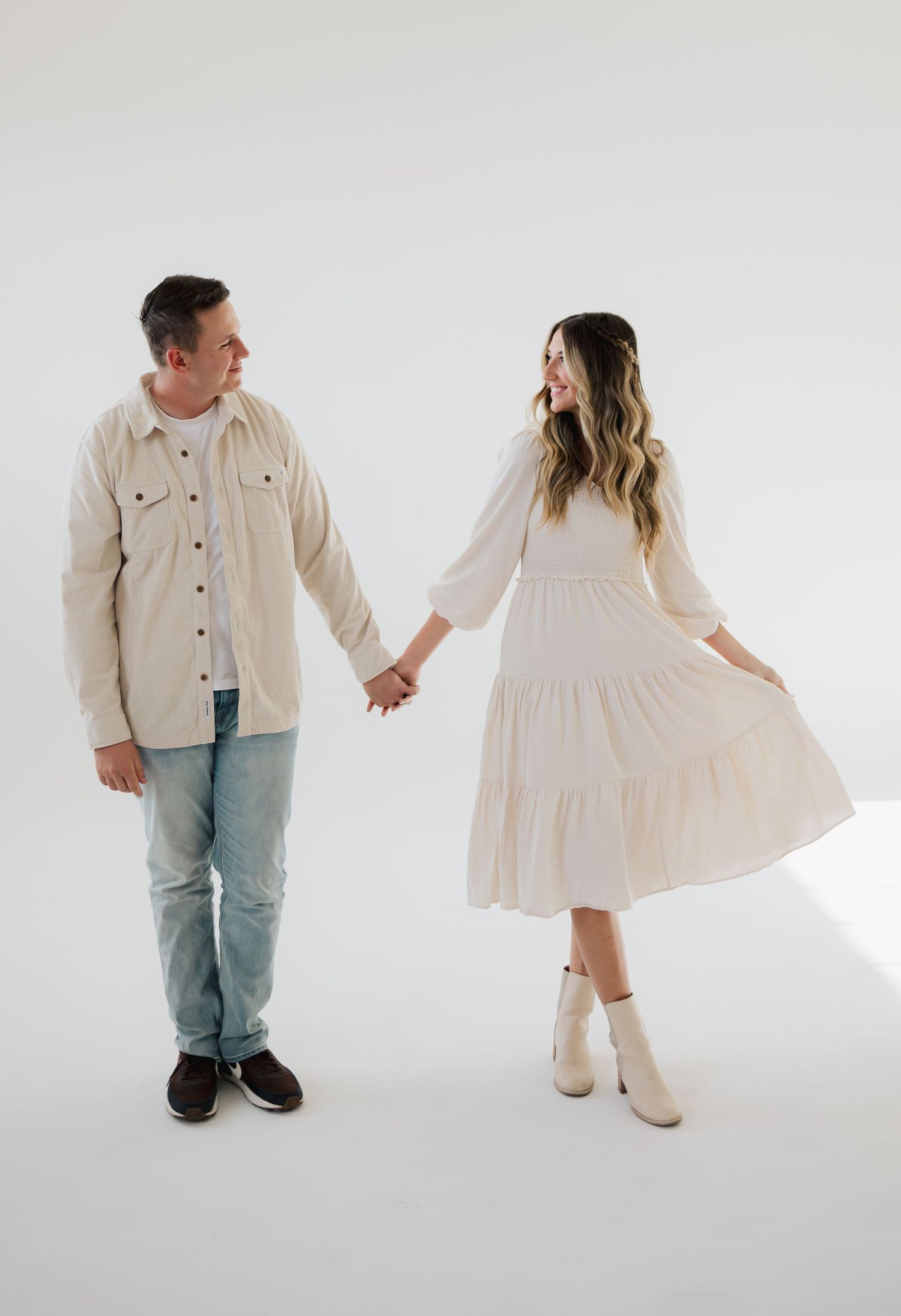 Couple wearing casual cream and beige outfits posing playfully against white studio backdrop in series of photos.