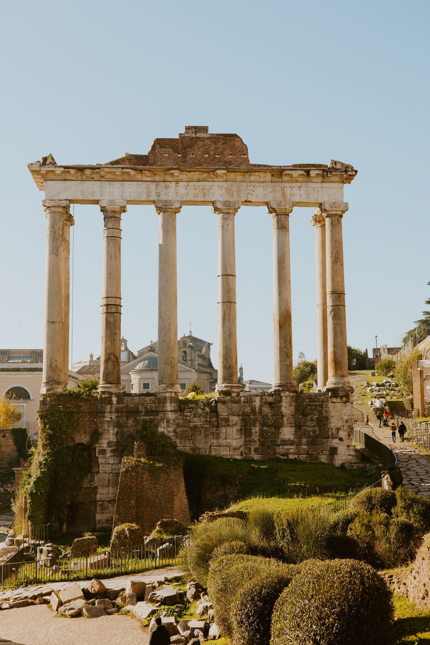 Ancient Roman Temple of Saturn ruins with tall ionic columns standing against a clear blue sky in the Roman Forum, Italy.