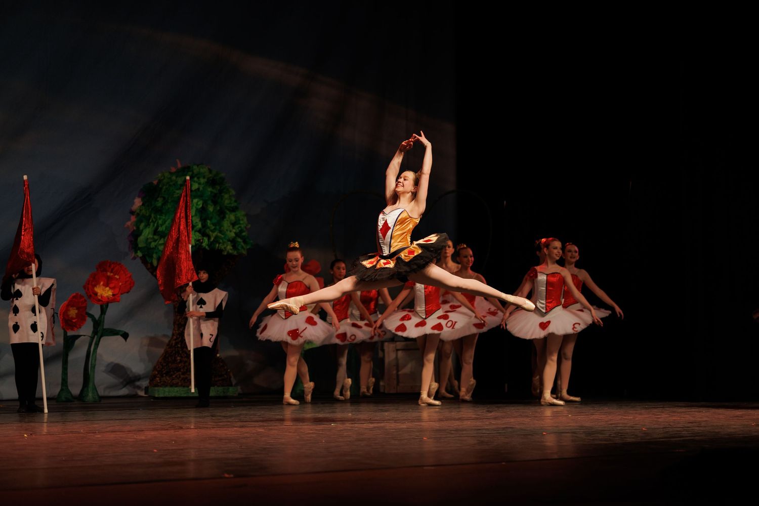 Ballet dancers perform graceful movements during a stage performance with red and green lighting effects.