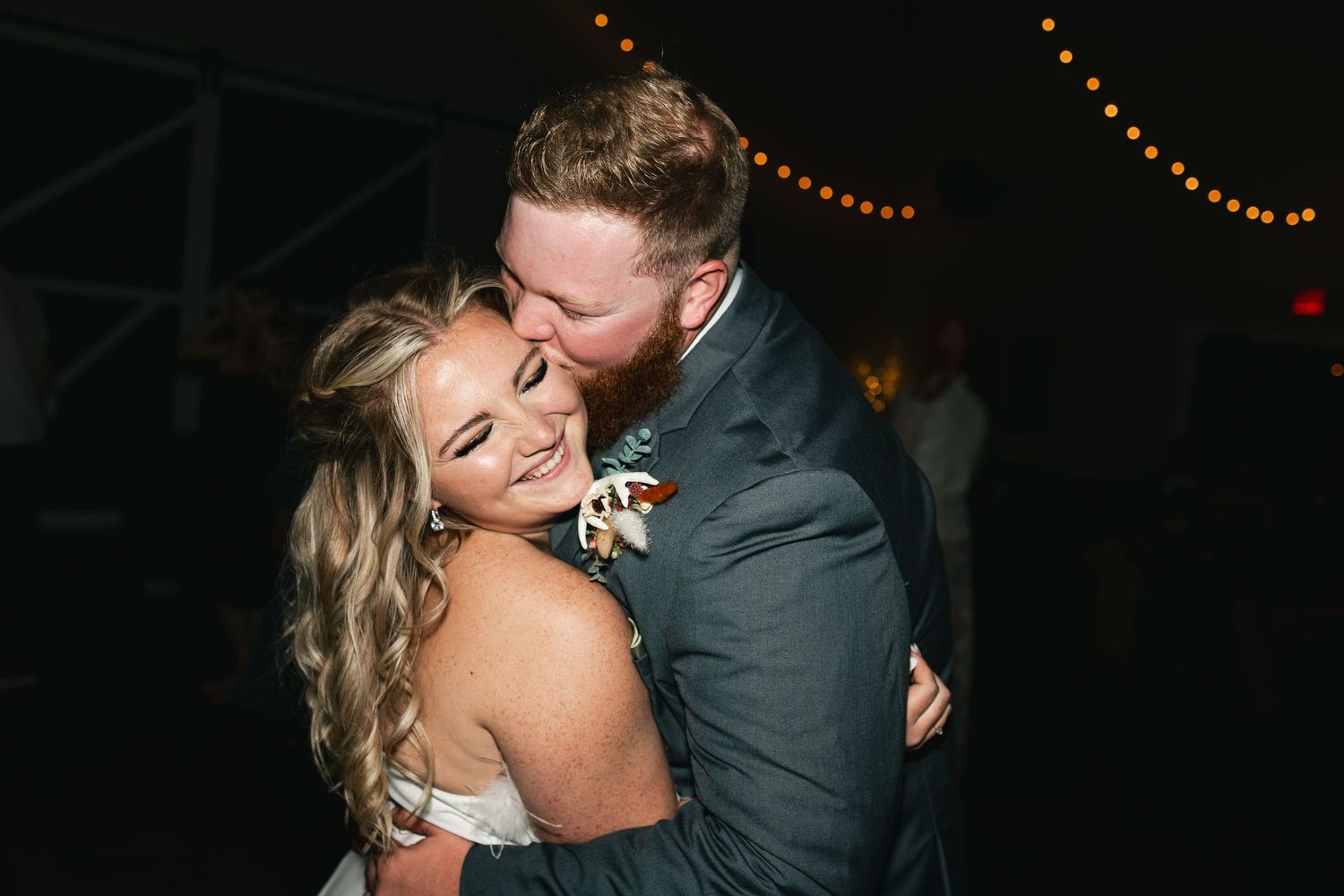 Couple shares an intimate dance moment under twinkling string lights at their wedding reception.