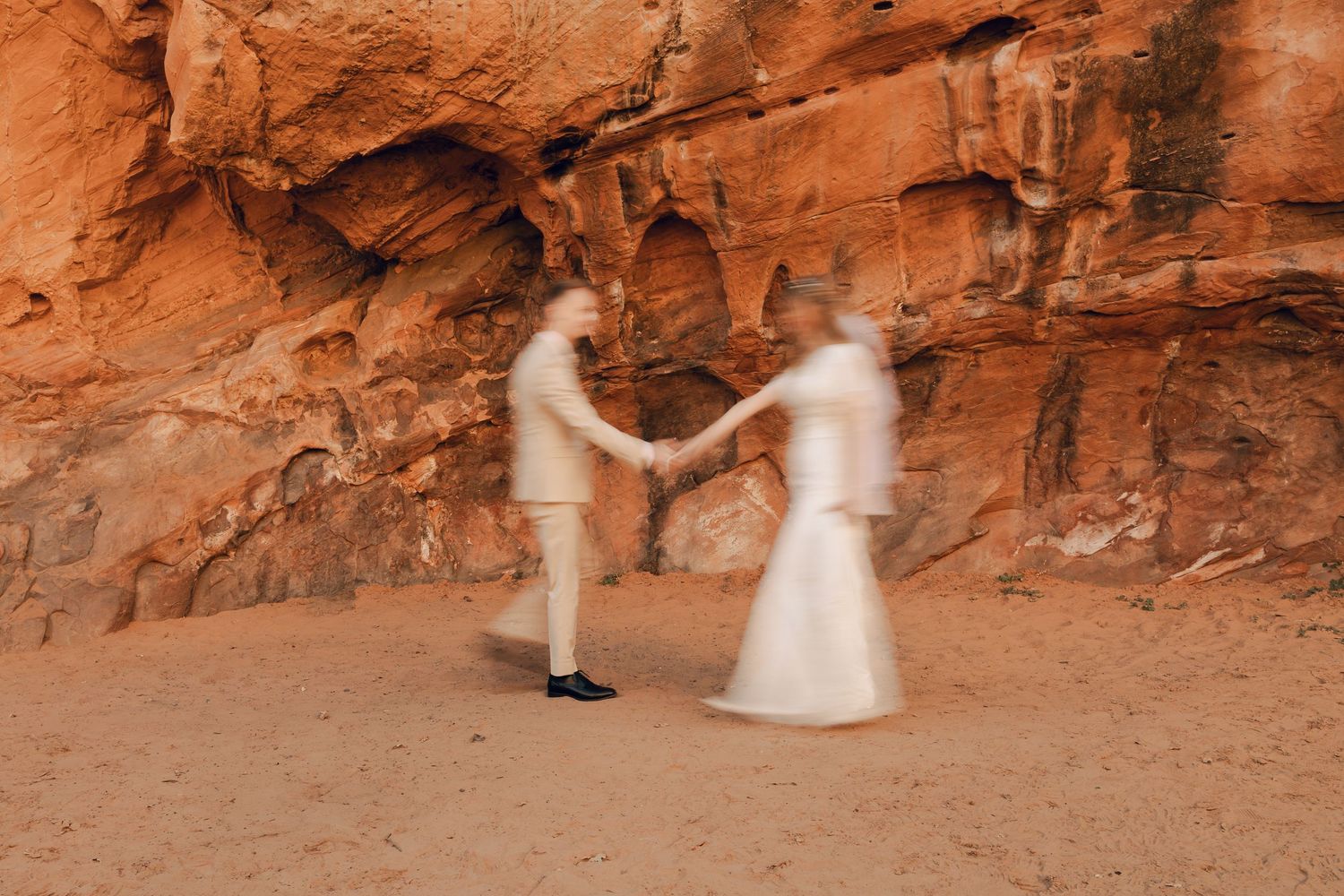 A wedding couple twirls against dramatic red rock formations in a desert landscape.