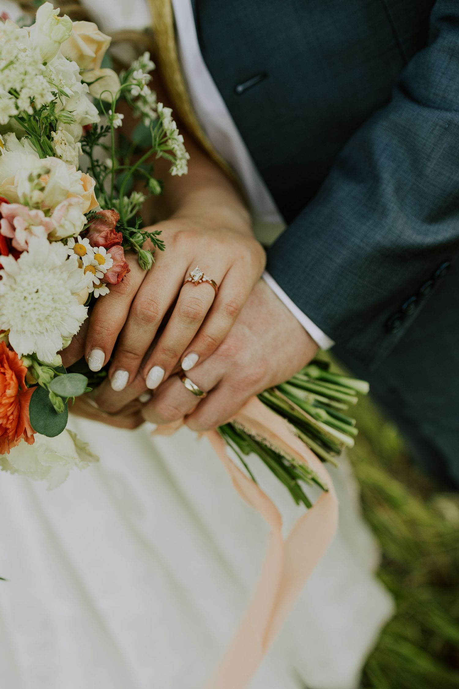 Close up of hands holding a white and orange wedding bouquet with delicate flowers and greenery accents.