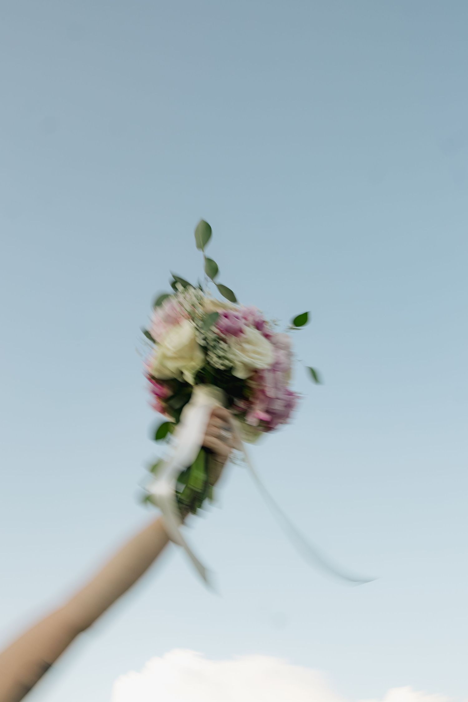 A blurred motion shot of a wedding bouquet being tossed against a blue sky.