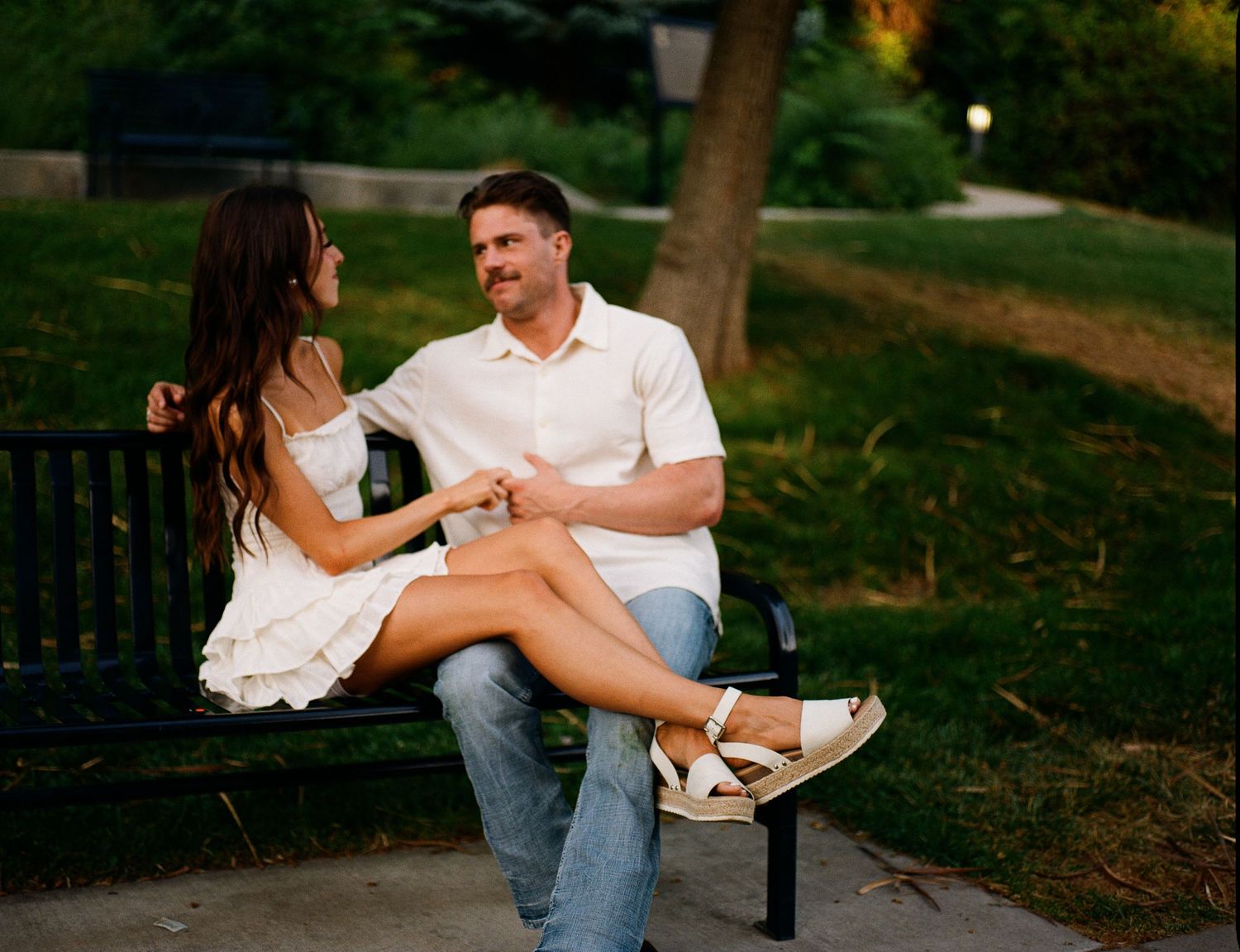 A couple sits together on park benches during a warm summer evening, sharing laughter and conversation.