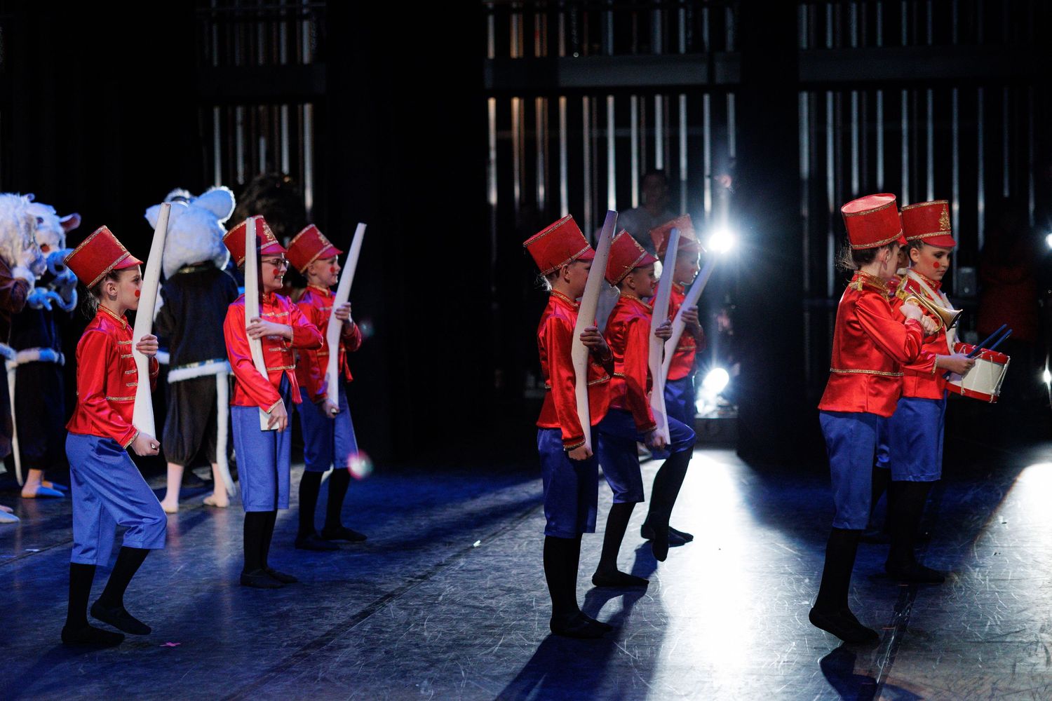 Dancers in red and blue costumes move dramatically across a dimly lit stage during a performance.