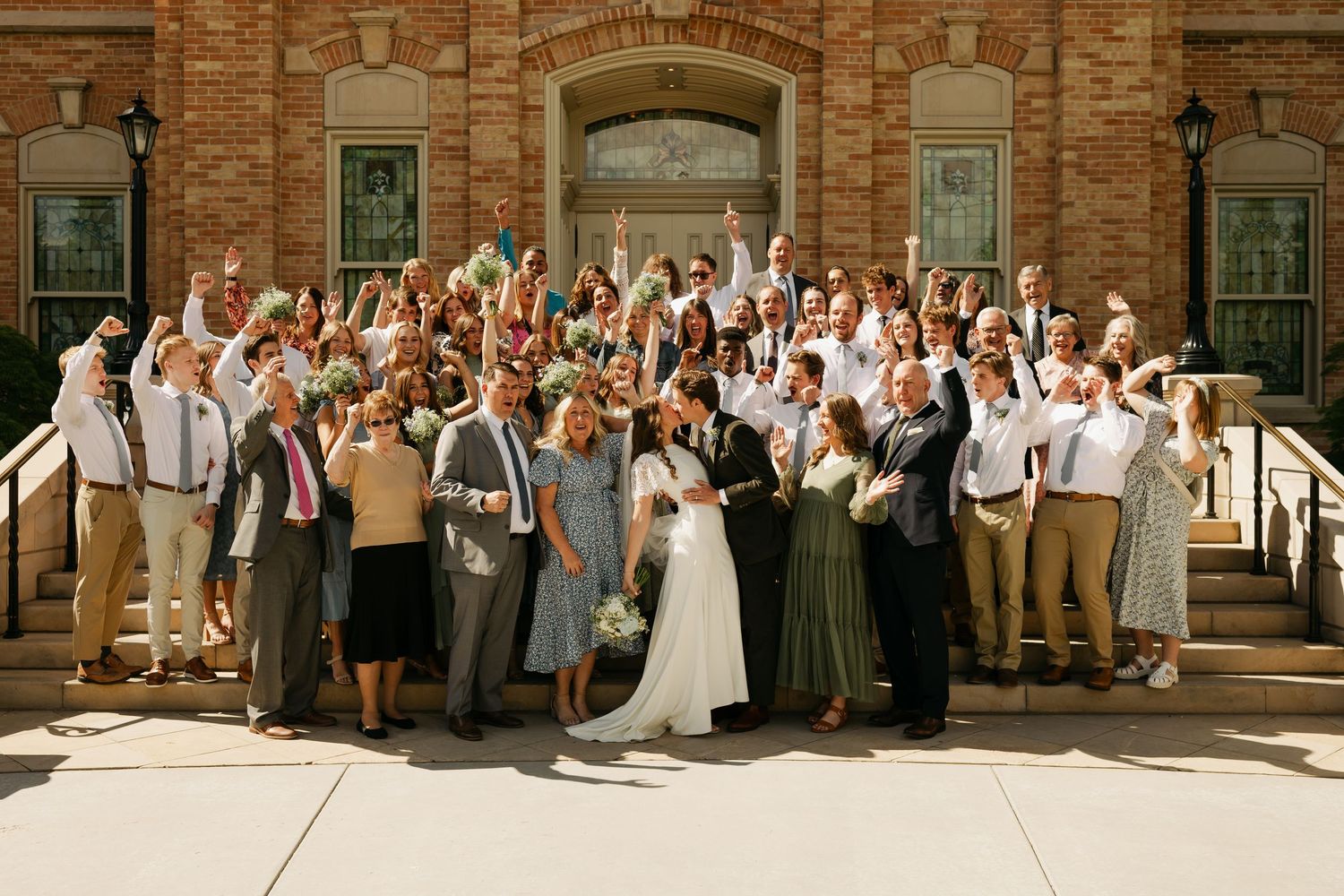 Large wedding party poses together outside a historic brick building.