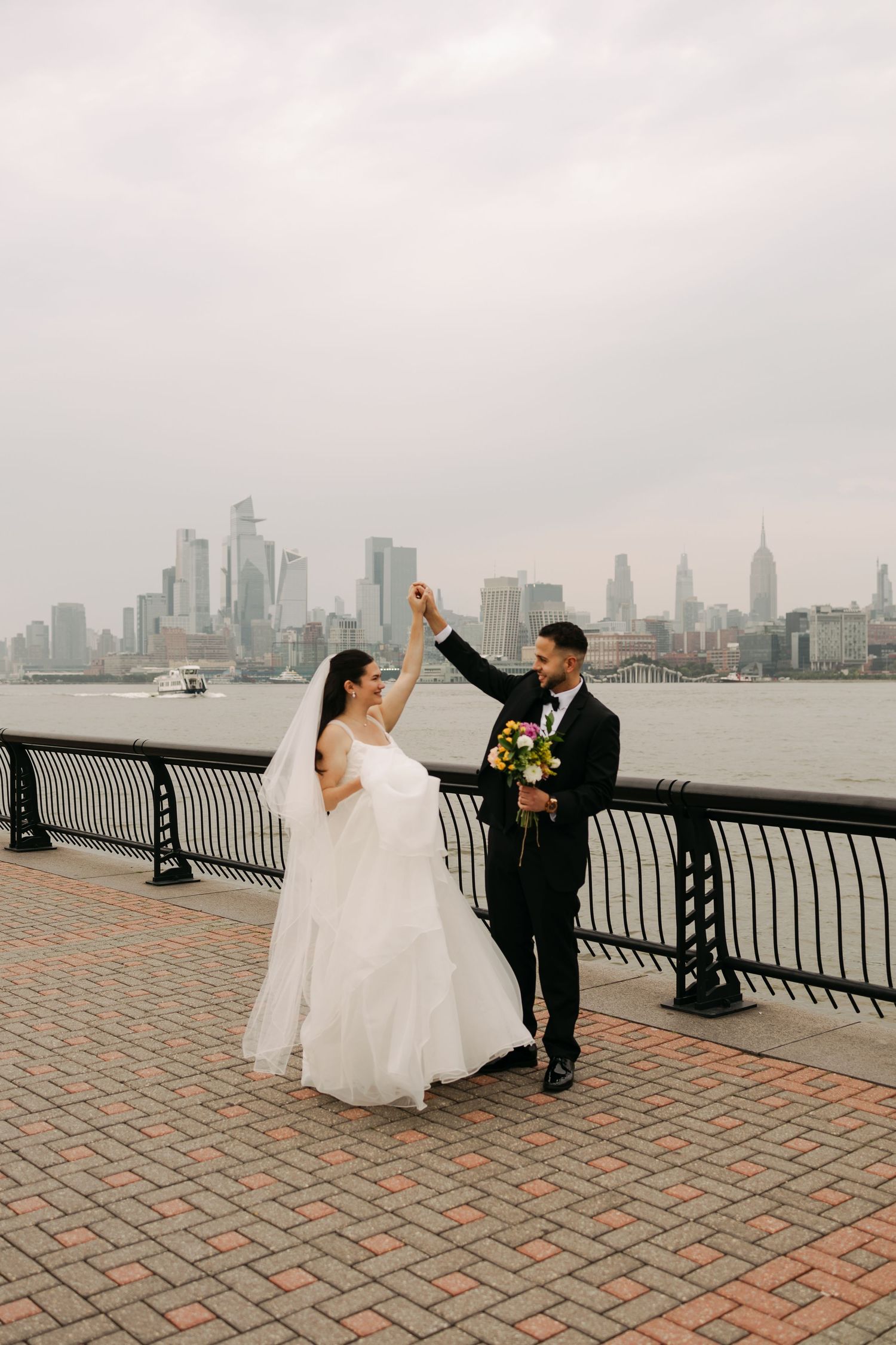 Wedding couple shares a romantic dance along the waterfront with the New York City skyline in the background.