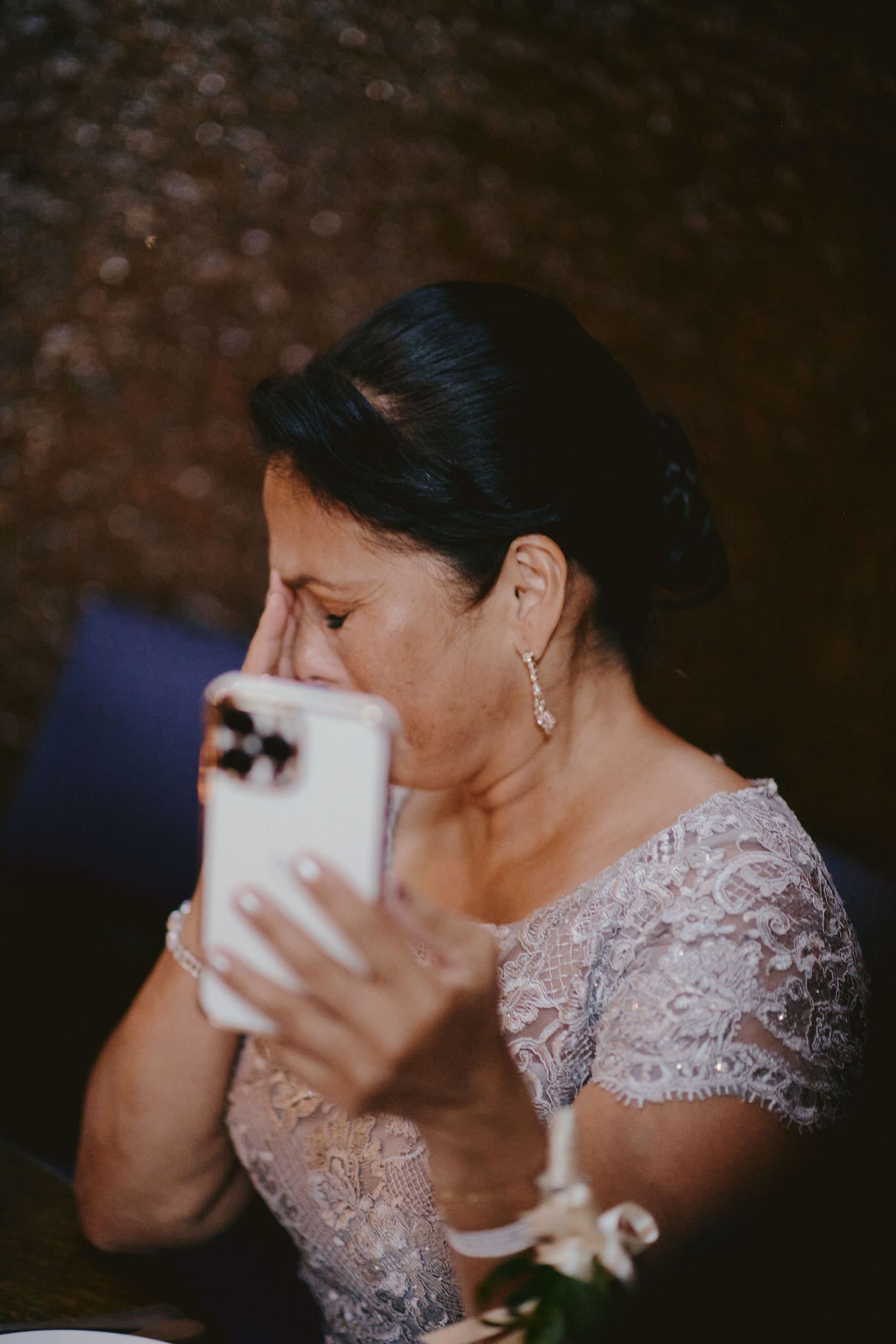 Someone in an elegant lace dress wipes their eyes with emotion at a wedding reception.