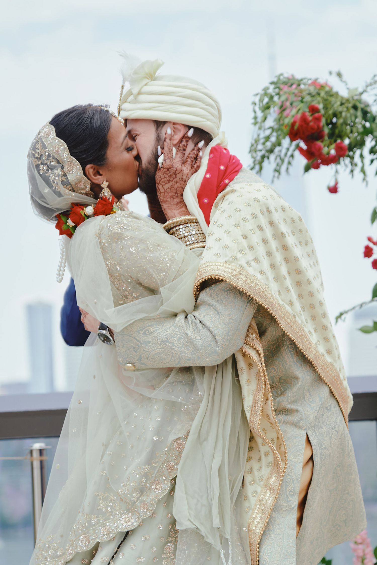 A couple shares a romantic kiss during their traditional Indian wedding celebration, dressed in elegant cream and gold attire.