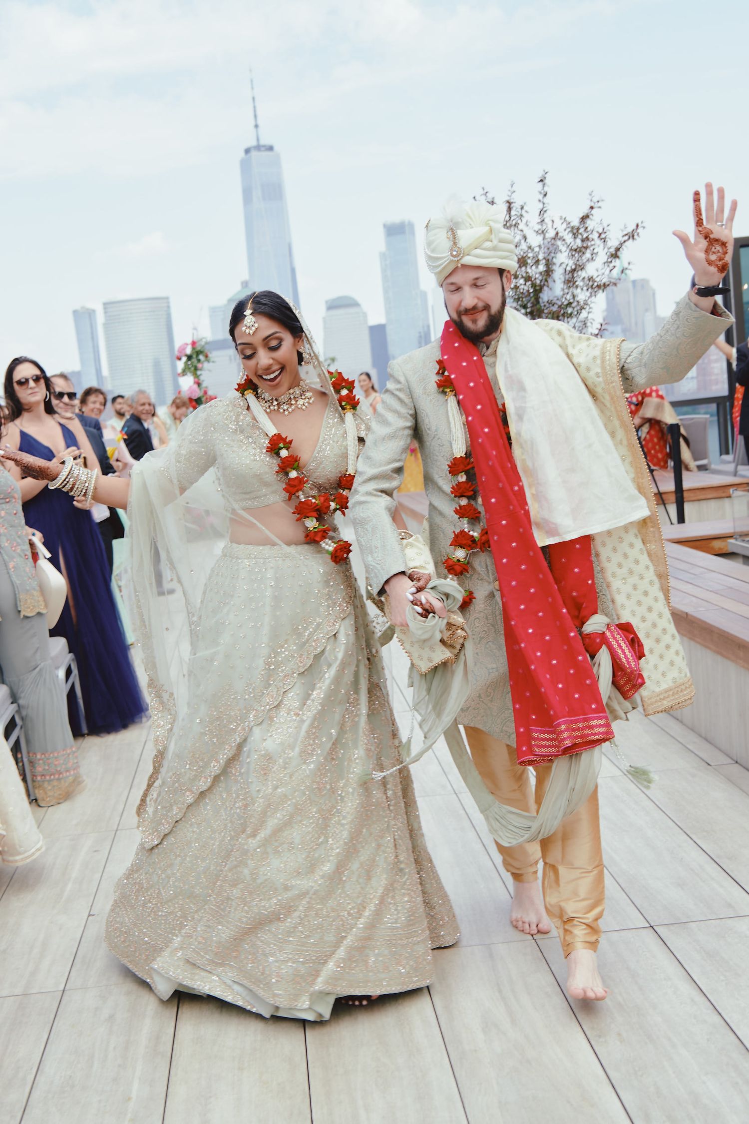 A couple celebrates their wedding in traditional Indian attire with the New York City skyline visible in the background.