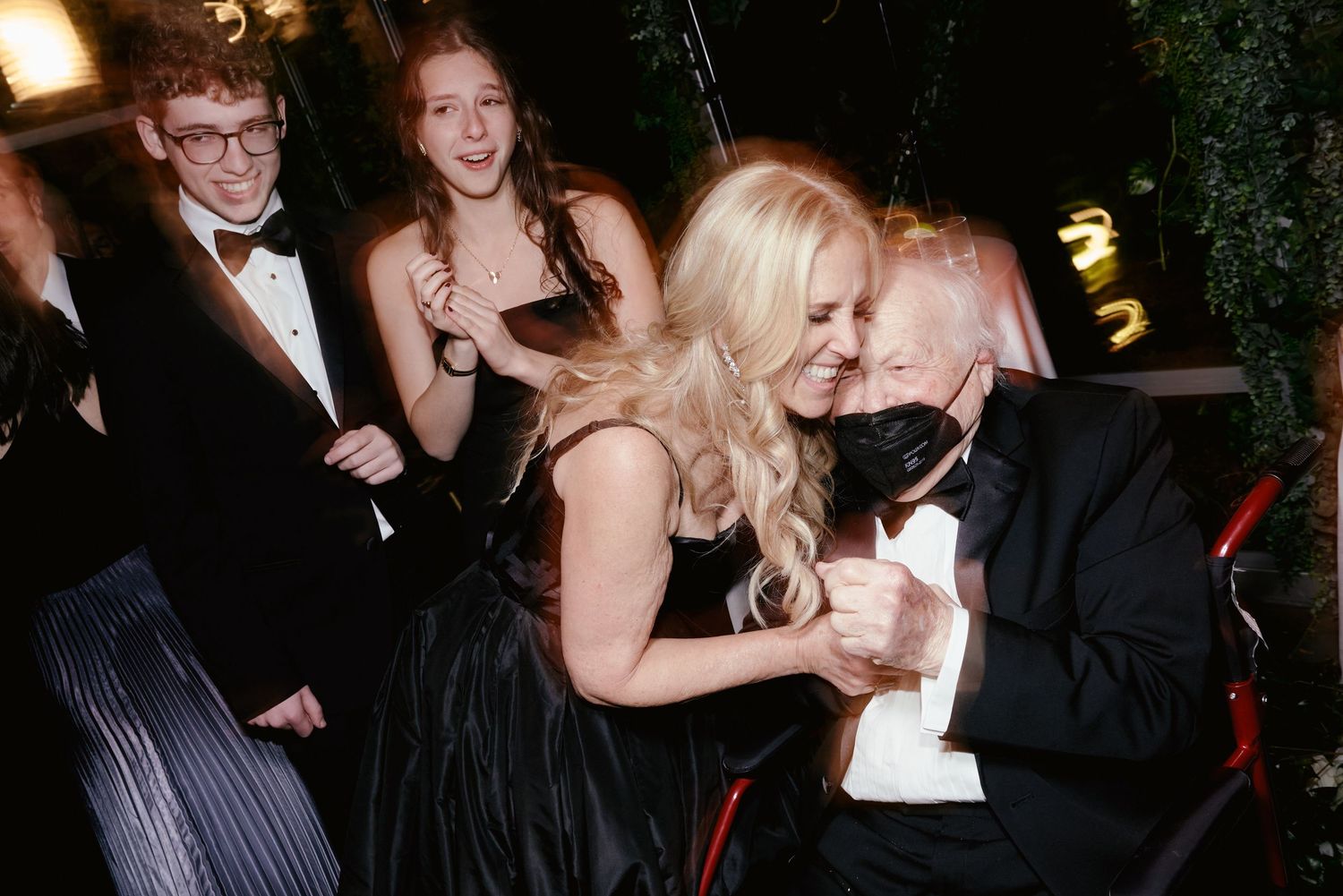 A celebratory scene at a formal event shows people in evening wear laughing and enjoying themselves at a gathering.