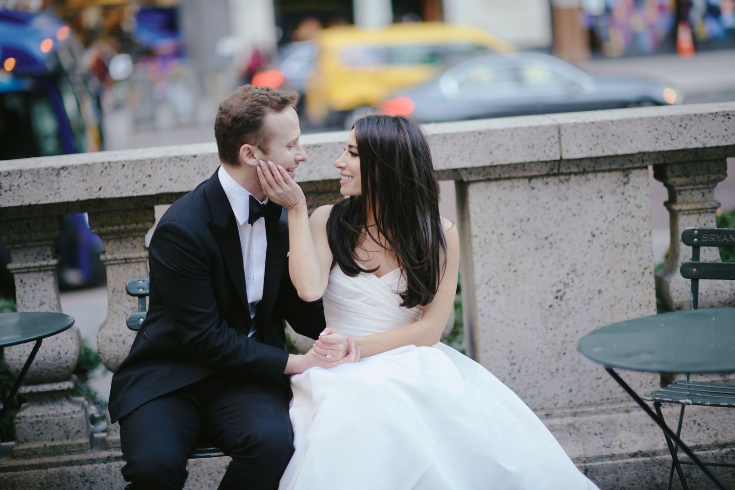 A romantic moment between a couple in wedding attire sitting on stone steps in a city setting.